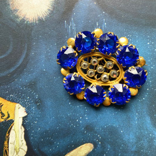 A brooch featuring a vivid, ultramarine blue glass stone that draws the eye with its deep, striking colour. ウルトラマリンのような深く鮮やかなブルーが印象的な、グラスストーンのブローチ。 