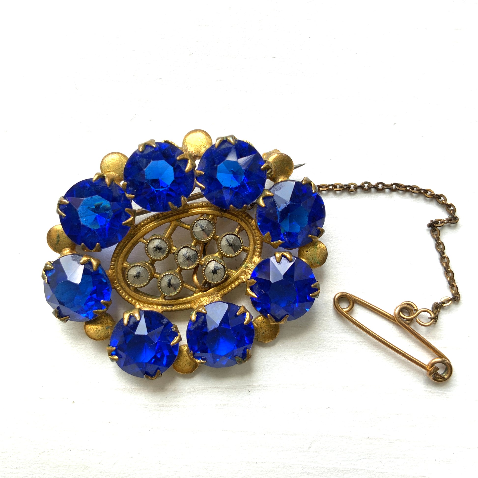 A brooch featuring a vivid, ultramarine blue glass stone that draws the eye with its deep, striking colour. ウルトラマリンのような深く鮮やかなブルーが印象的な、グラスストーンのブローチ。 