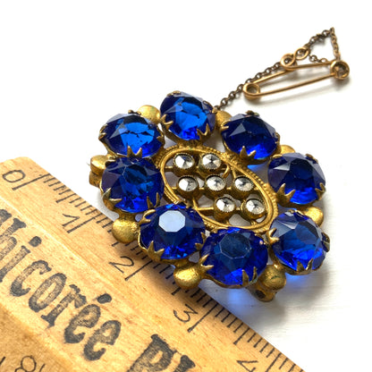 A brooch featuring a vivid, ultramarine blue glass stone that draws the eye with its deep, striking colour. ウルトラマリンのような深く鮮やかなブルーが印象的な、グラスストーンのブローチ。 