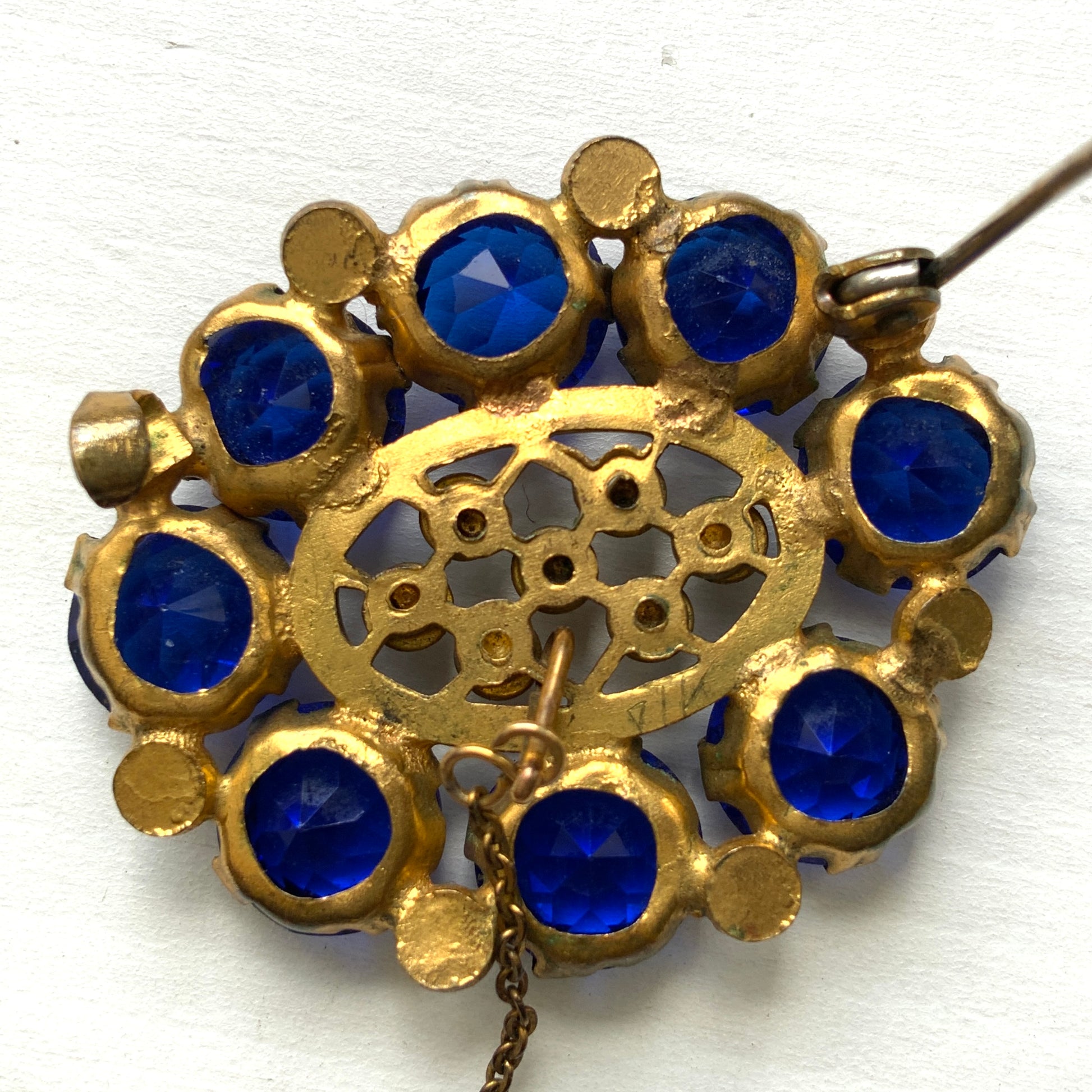 A brooch featuring a vivid, ultramarine blue glass stone that draws the eye with its deep, striking colour. ウルトラマリンのような深く鮮やかなブルーが印象的な、グラスストーンのブローチ。 