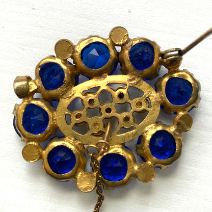 A brooch featuring a vivid, ultramarine blue glass stone that draws the eye with its deep, striking colour. ウルトラマリンのような深く鮮やかなブルーが印象的な、グラスストーンのブローチ。 