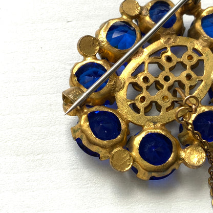 A brooch featuring a vivid, ultramarine blue glass stone that draws the eye with its deep, striking colour. ウルトラマリンのような深く鮮やかなブルーが印象的な、グラスストーンのブローチ。 