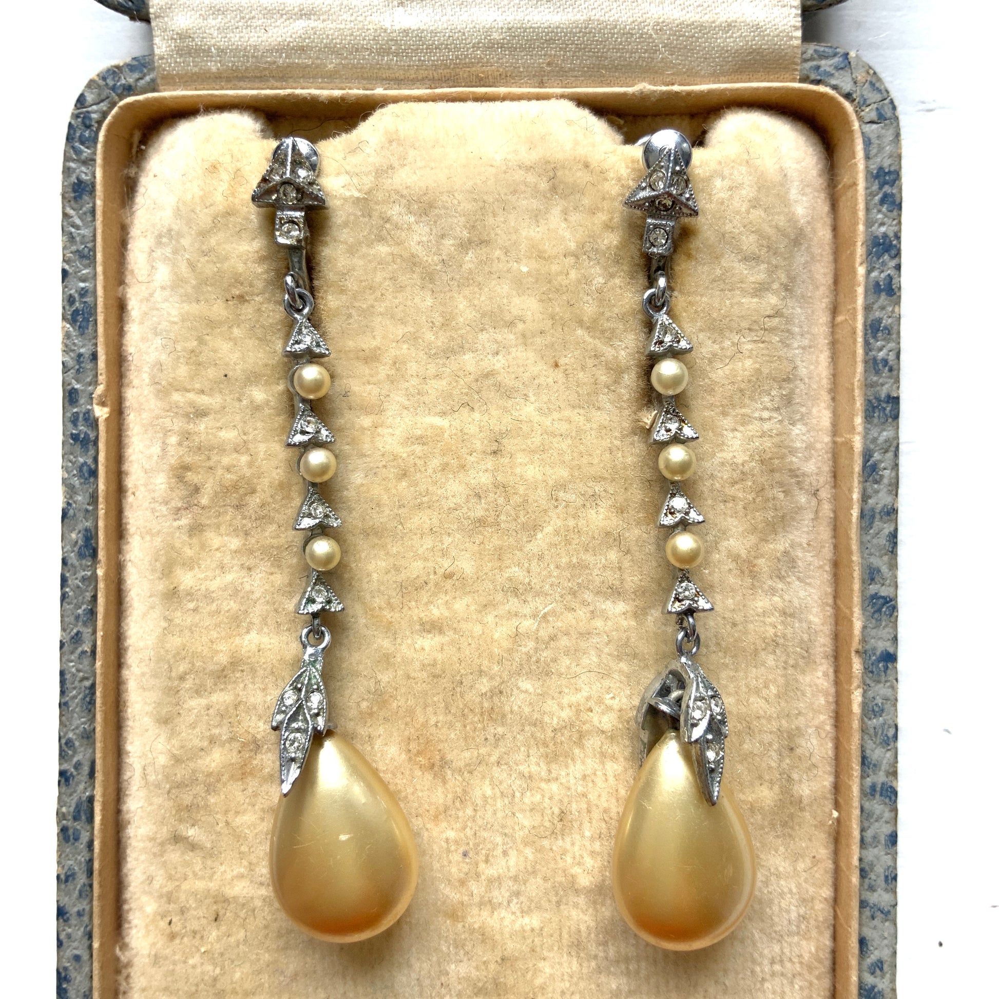 Screw earrings featuring a silver-tone leaf with a champagne gold teardrop pearl glass dangling from the tip. シルバートーンのリーフの先にシャンパンゴールドカラーのティアドロップグラスパールが揺れるスクリューイヤリング。