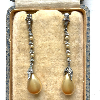Screw earrings featuring a silver-tone leaf with a champagne gold teardrop pearl glass dangling from the tip. シルバートーンのリーフの先にシャンパンゴールドカラーのティアドロップグラスパールが揺れるスクリューイヤリング。