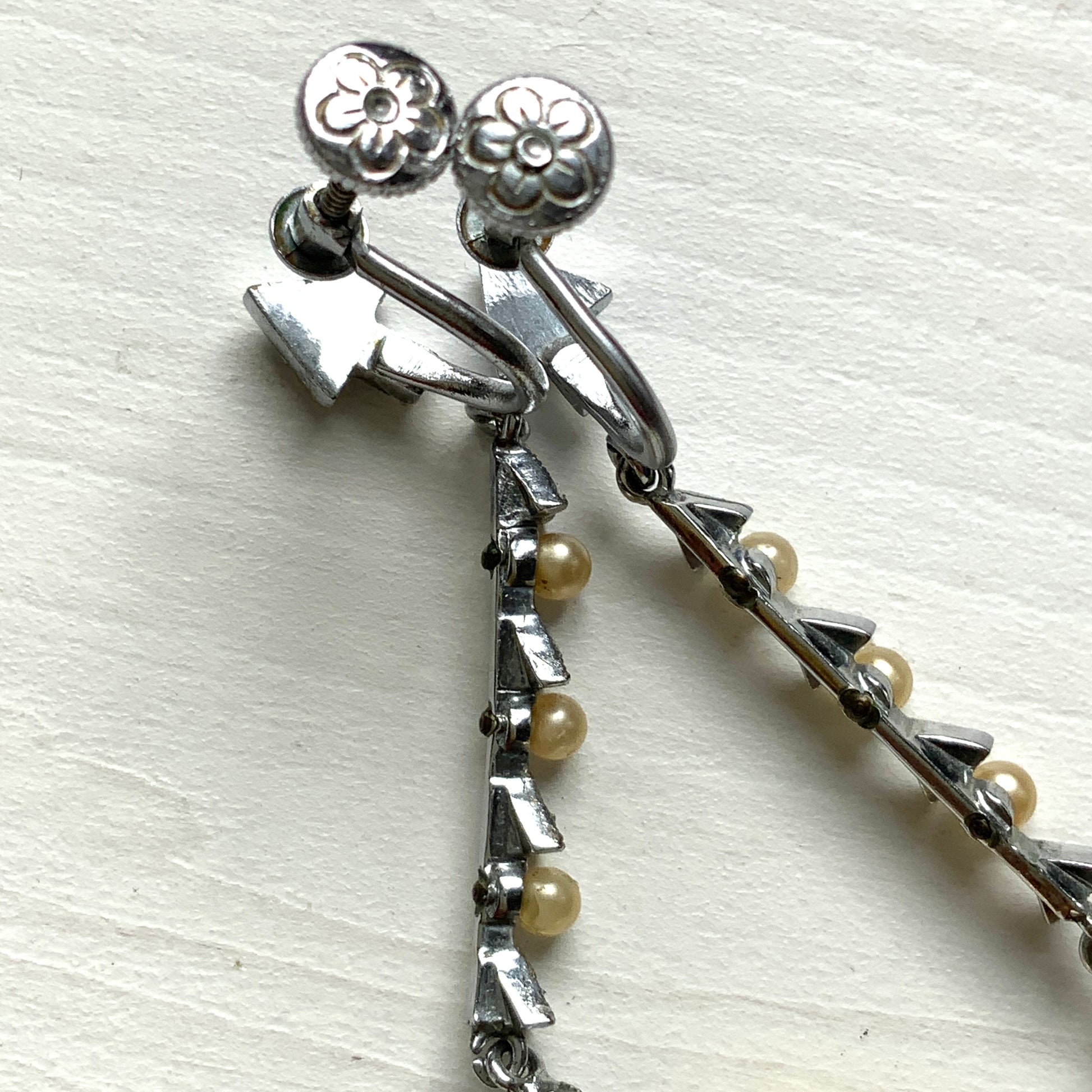 Screw earrings featuring a silver-tone leaf with a champagne gold teardrop pearl glass dangling from the tip. シルバートーンのリーフの先にシャンパンゴールドカラーのティアドロップグラスパールが揺れるスクリューイヤリング。