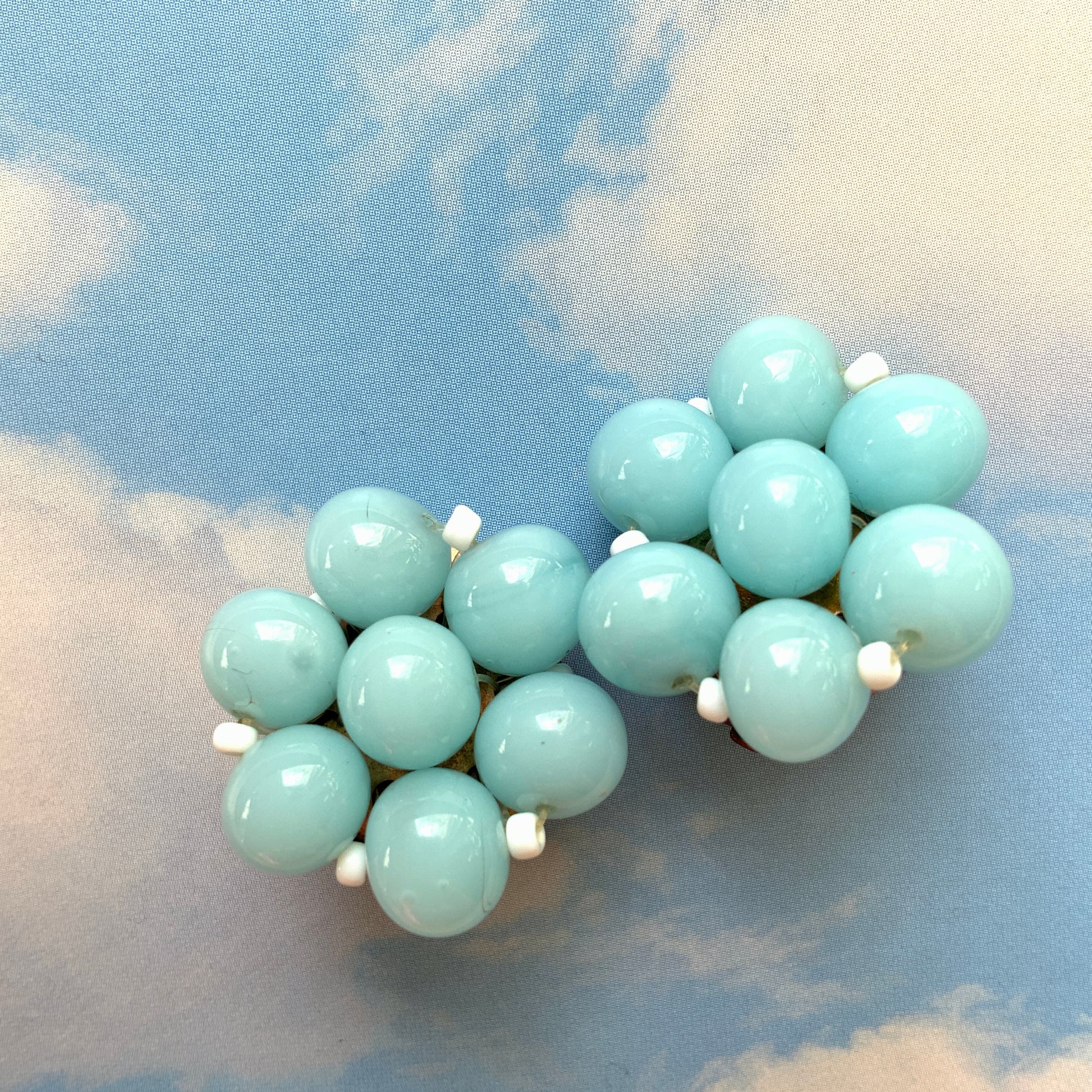 These clip-on earrings feature a cluster of soft pastel blue glass beads, accented with small milk glass beads nestled in between. 淡いパステルブルーのガラスビーズが集まったクリップイヤリング。