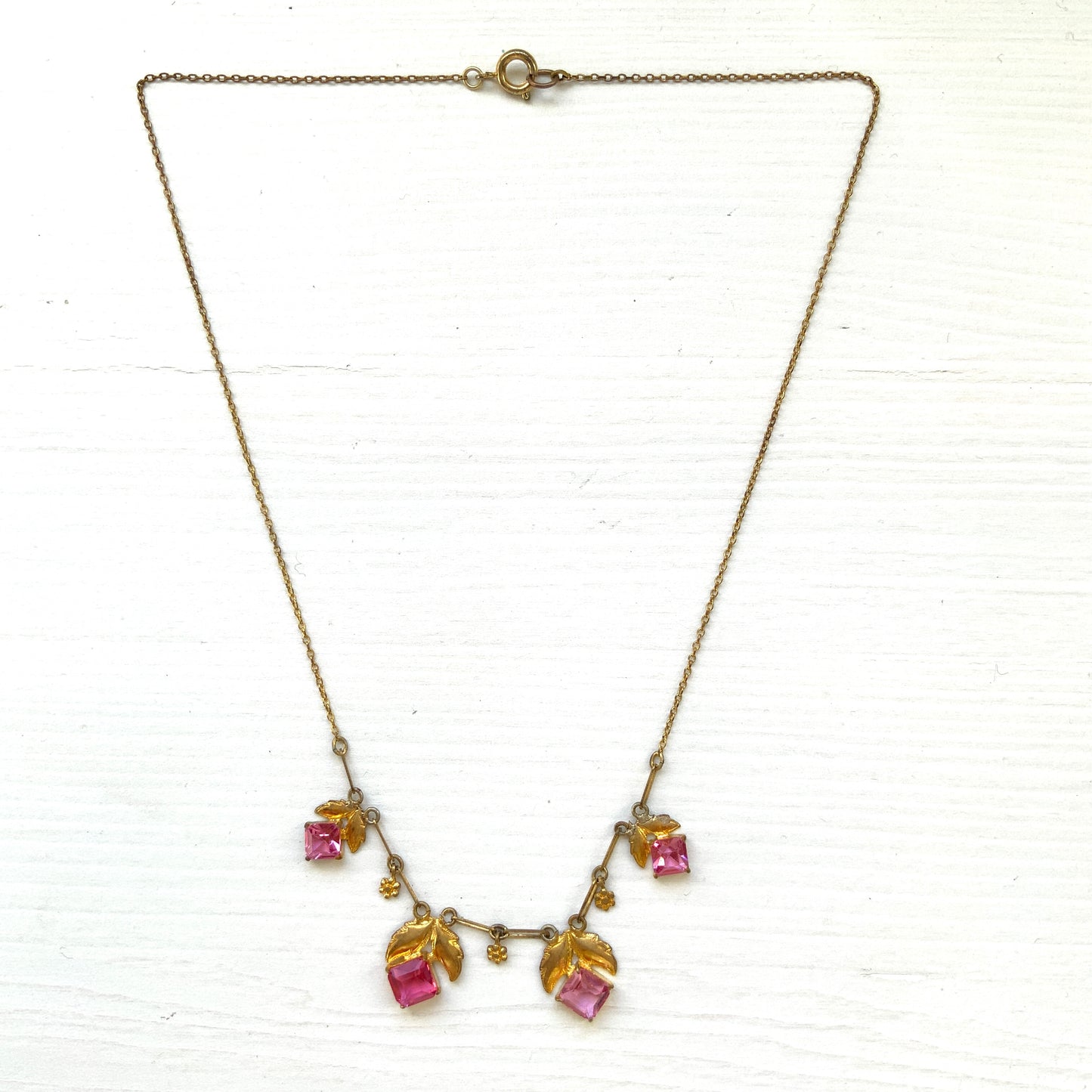 A delicate necklace featuring gold-tone leaves set with pink square glass stones. ゴールドトーンのリーフにピンクのスクエアガラスをあしらったネックレス。