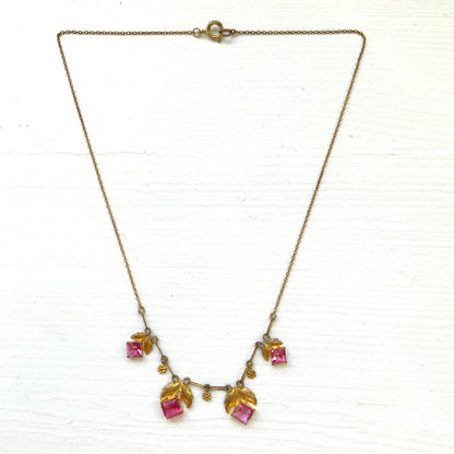 A delicate necklace featuring gold-tone leaves set with pink square glass stones. ゴールドトーンのリーフにピンクのスクエアガラスをあしらったネックレス。