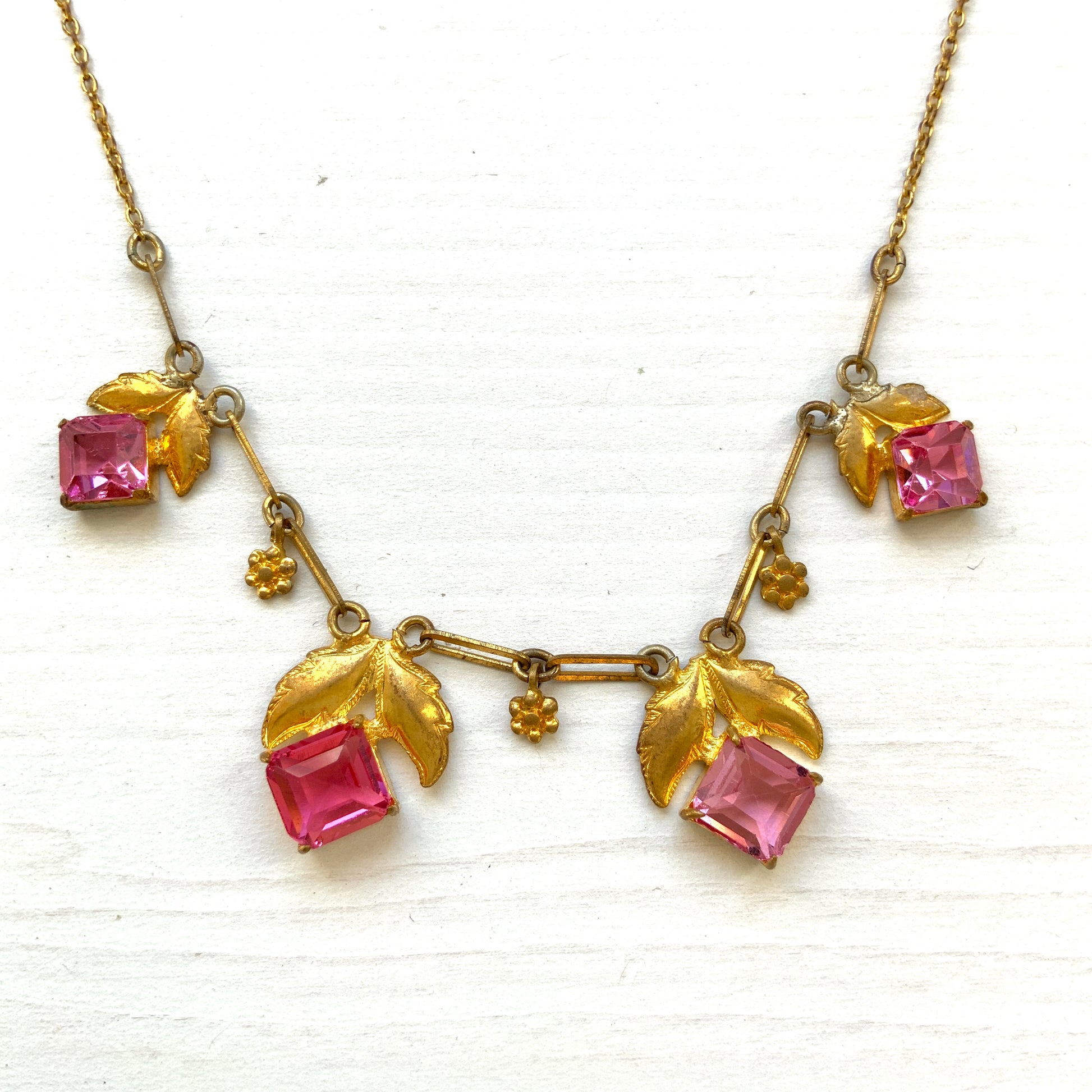 A delicate necklace featuring gold-tone leaves set with pink square glass stones. ゴールドトーンのリーフにピンクのスクエアガラスをあしらったネックレス。