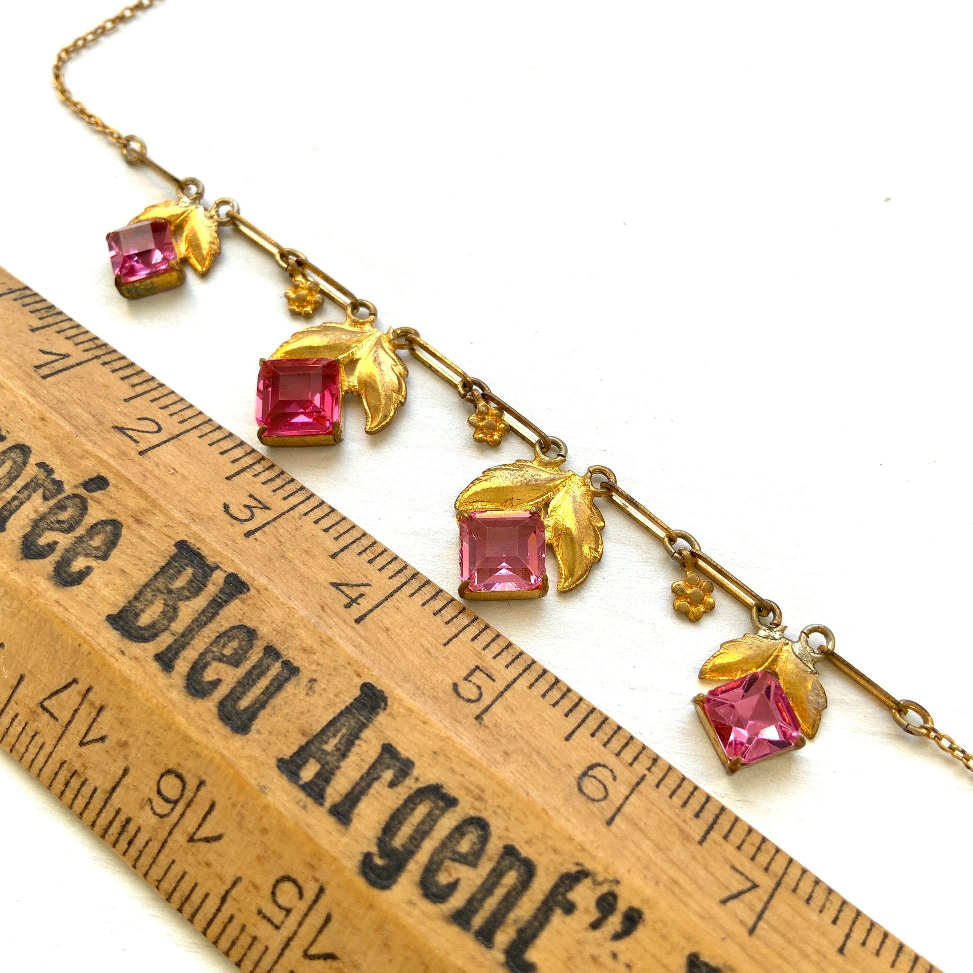A delicate necklace featuring gold-tone leaves set with pink square glass stones. ゴールドトーンのリーフにピンクのスクエアガラスをあしらったネックレス。