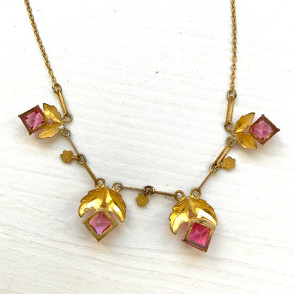 A delicate necklace featuring gold-tone leaves set with pink square glass stones. ゴールドトーンのリーフにピンクのスクエアガラスをあしらったネックレス。