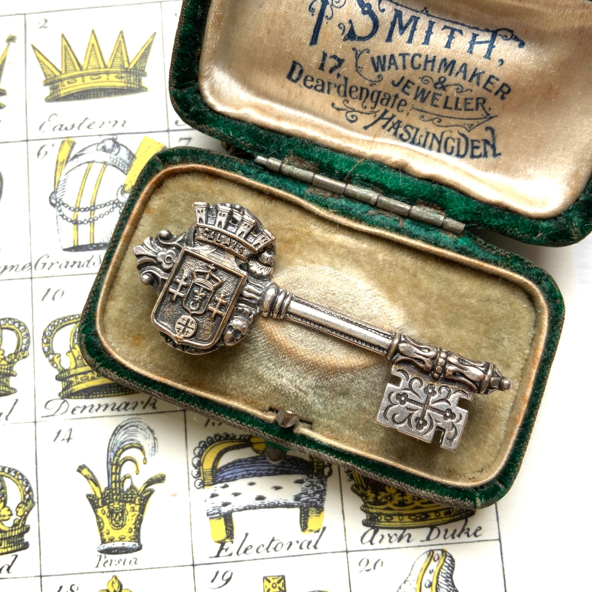 A decorative vintage key brooch featuring a crown and crest motif in a beautifully classical design. 王冠と紋章のモチーフ、クラシカルでデコラティブなデザインが素敵な鍵ブローチ。 