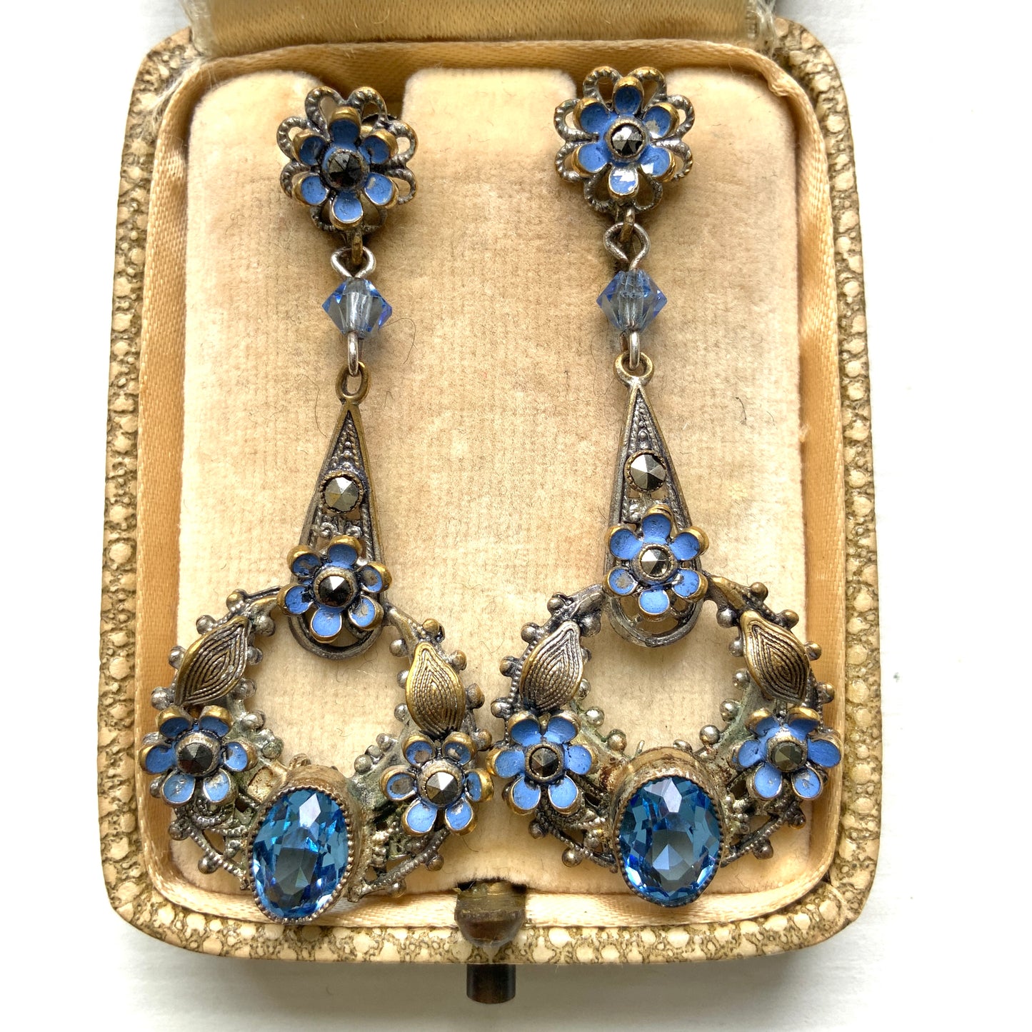 Screw-back earrings featuring pale blue enamel flowers and glass bijoux. Delicately crafted in a crescent-shaped filigree, the tiny enamel blossoms sparkle alongside drops of soft, water-like blue glass stones. 淡いブルーのエナメルフラワーとグラスビジューのスクリューイヤリング。 三日月型の繊細なフィリグリーに、小さなエナメルの花々と、水の雫のように澄んだブルーグラスがきらめきます。 