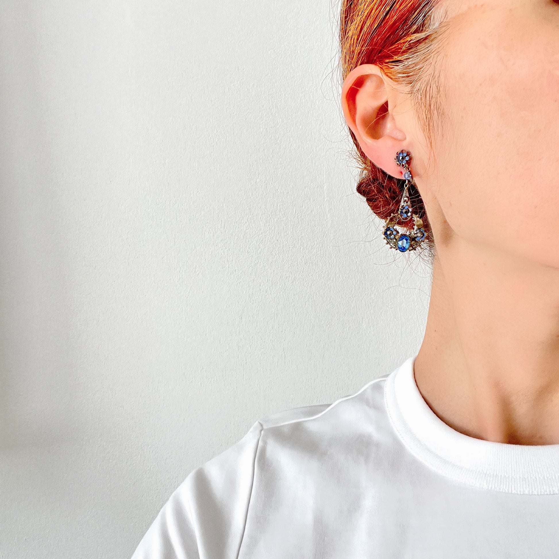 Screw-back earrings featuring pale blue enamel flowers and glass bijoux. Delicately crafted in a crescent-shaped filigree, the tiny enamel blossoms sparkle alongside drops of soft, water-like blue glass stones. 淡いブルーのエナメルフラワーとグラスビジューのスクリューイヤリング。 三日月型の繊細なフィリグリーに、小さなエナメルの花々と、水の雫のように澄んだブルーグラスがきらめきます。 