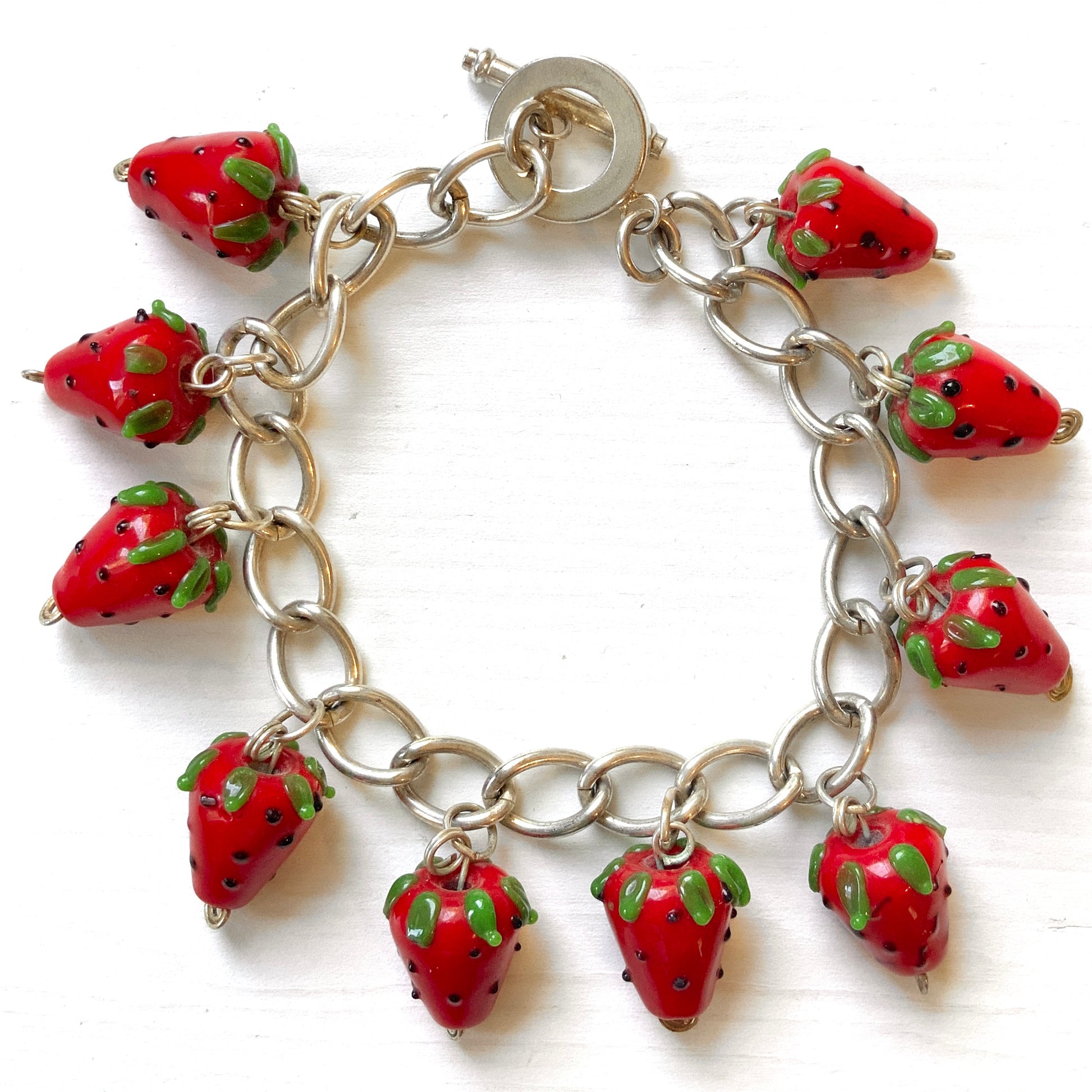 A bracelet with glass strawberry charms that sway from a silver-tone chain. ガラスのストロベリーチャームが揺れるブレスレット。