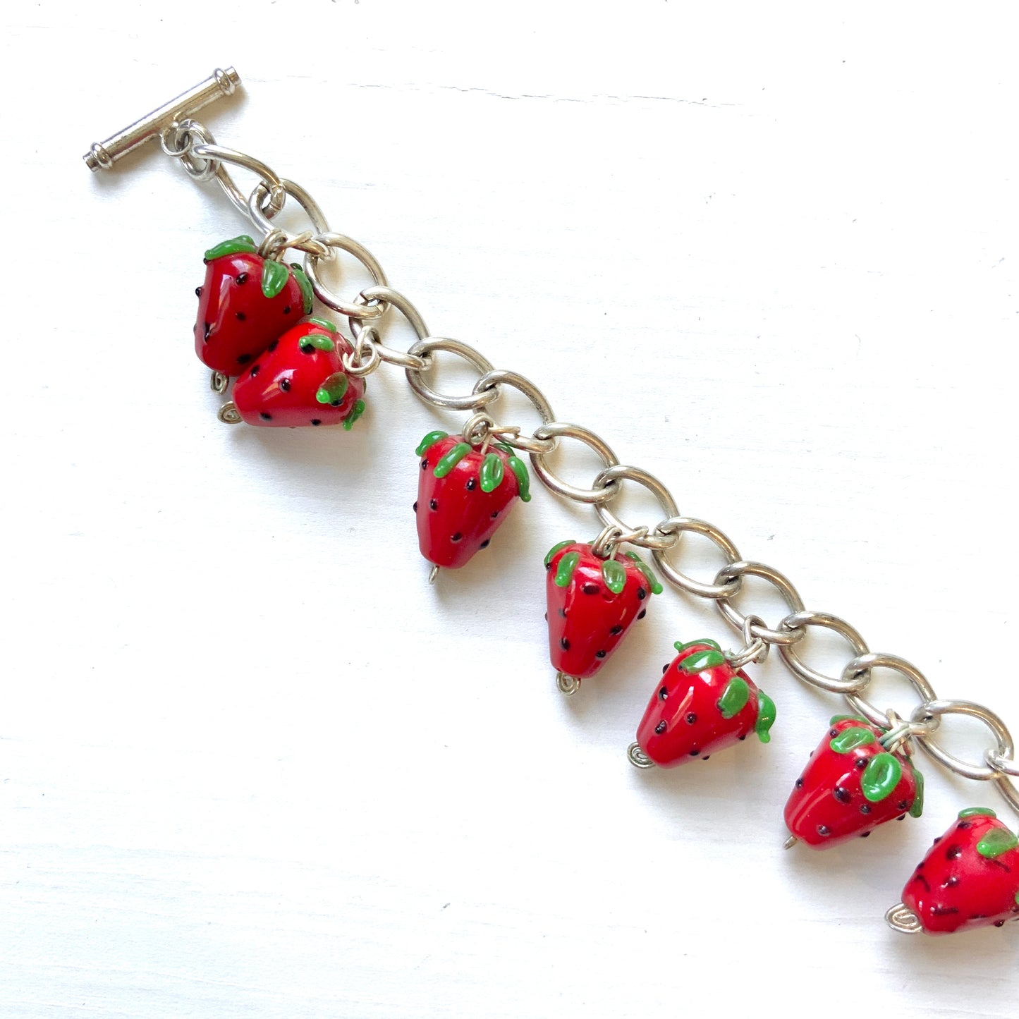 A bracelet with glass strawberry charms that sway from a silver-tone chain. ガラスのストロベリーチャームが揺れるブレスレット。