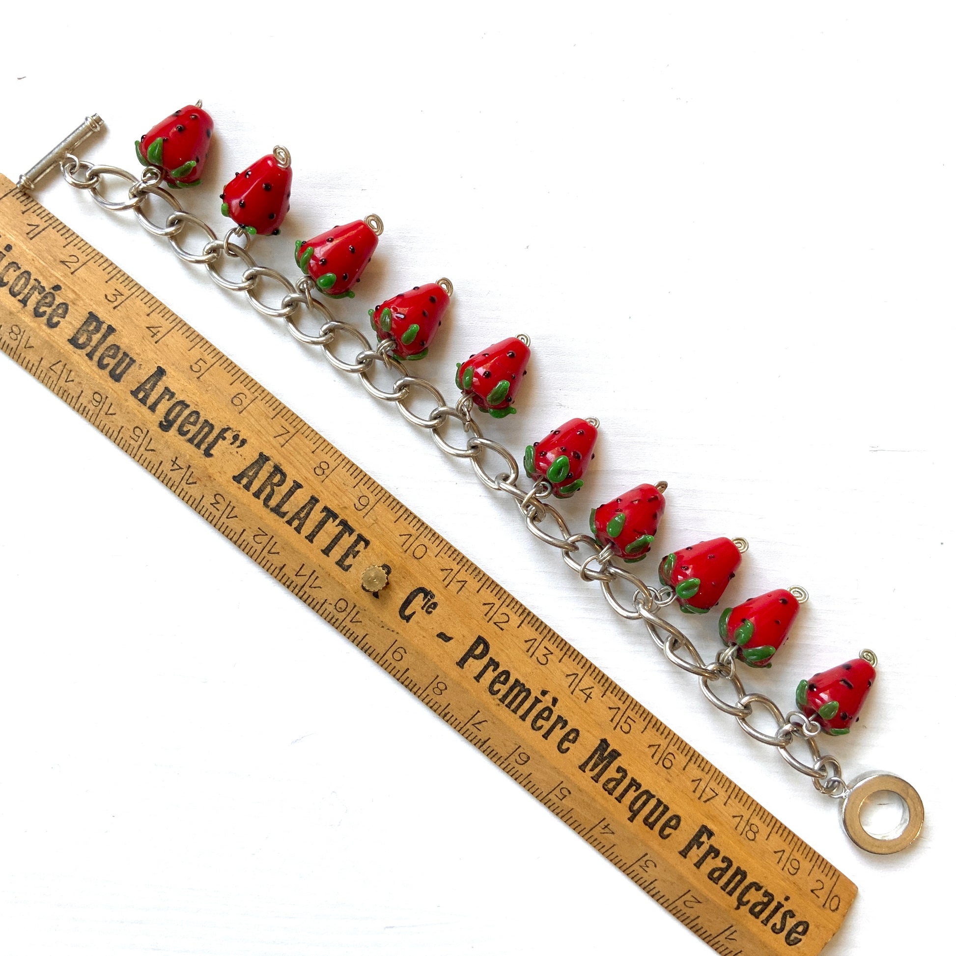 A bracelet with glass strawberry charms that sway from a silver-tone chain. ガラスのストロベリーチャームが揺れるブレスレット。