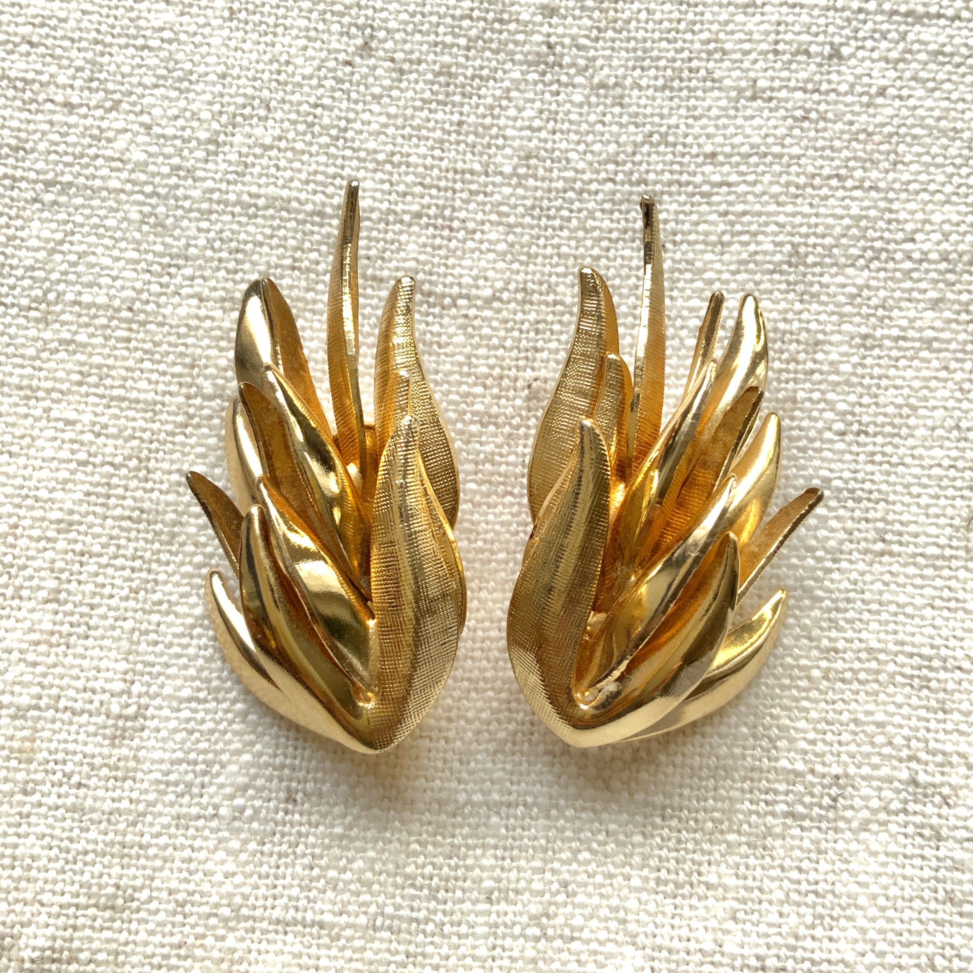 Gold-tone clip-on earrings featuring a sculptural, layered form reminiscent of feathers. 羽のように重なり合う立体的なフォルムが印象的な、ゴールドトーンのクリップイヤリング。