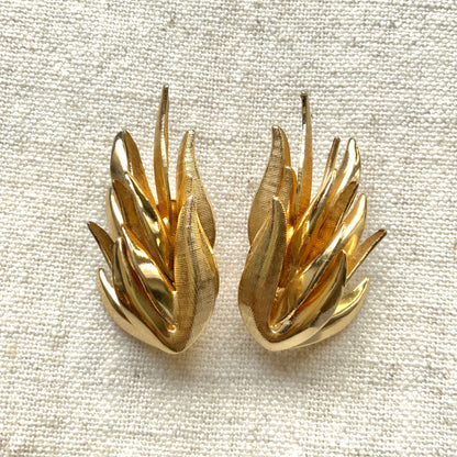 Gold-tone clip-on earrings featuring a sculptural, layered form reminiscent of feathers. 羽のように重なり合う立体的なフォルムが印象的な、ゴールドトーンのクリップイヤリング。