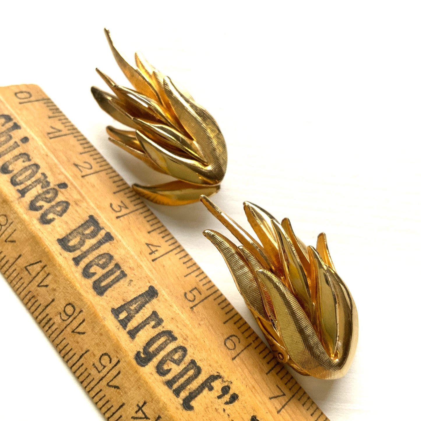 Gold-tone clip-on earrings featuring a sculptural, layered form reminiscent of feathers. 羽のように重なり合う立体的なフォルムが印象的な、ゴールドトーンのクリップイヤリング。