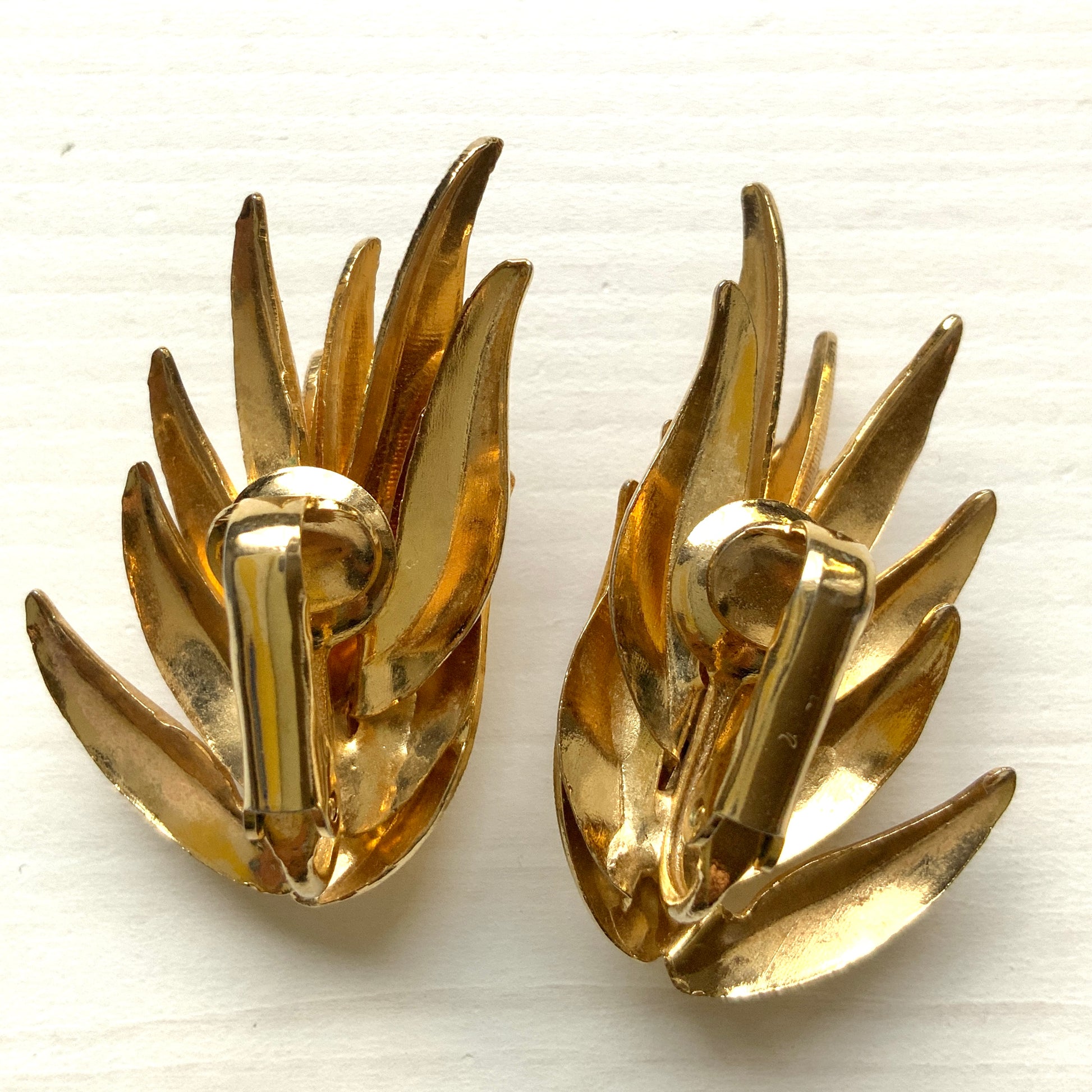 Gold-tone clip-on earrings featuring a sculptural, layered form reminiscent of feathers. 羽のように重なり合う立体的なフォルムが印象的な、ゴールドトーンのクリップイヤリング。