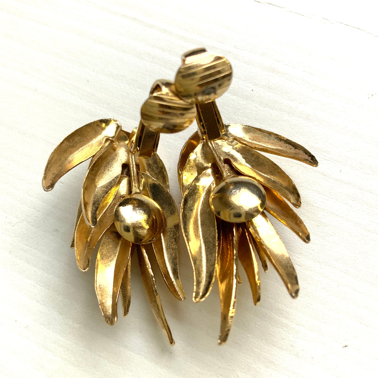 Gold-tone clip-on earrings featuring a sculptural, layered form reminiscent of feathers. 羽のように重なり合う立体的なフォルムが印象的な、ゴールドトーンのクリップイヤリング。