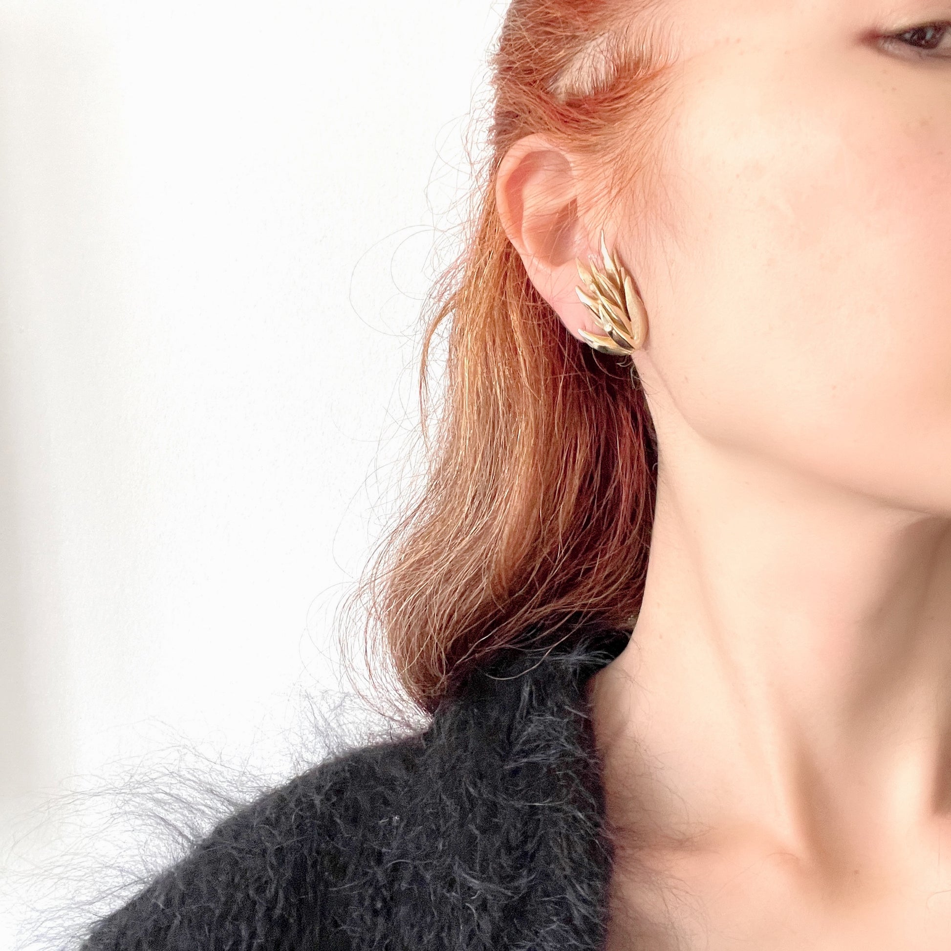 Gold-tone clip-on earrings featuring a sculptural, layered form reminiscent of feathers. 羽のように重なり合う立体的なフォルムが印象的な、ゴールドトーンのクリップイヤリング。
