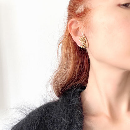 Gold-tone clip-on earrings featuring a sculptural, layered form reminiscent of feathers. 羽のように重なり合う立体的なフォルムが印象的な、ゴールドトーンのクリップイヤリング。