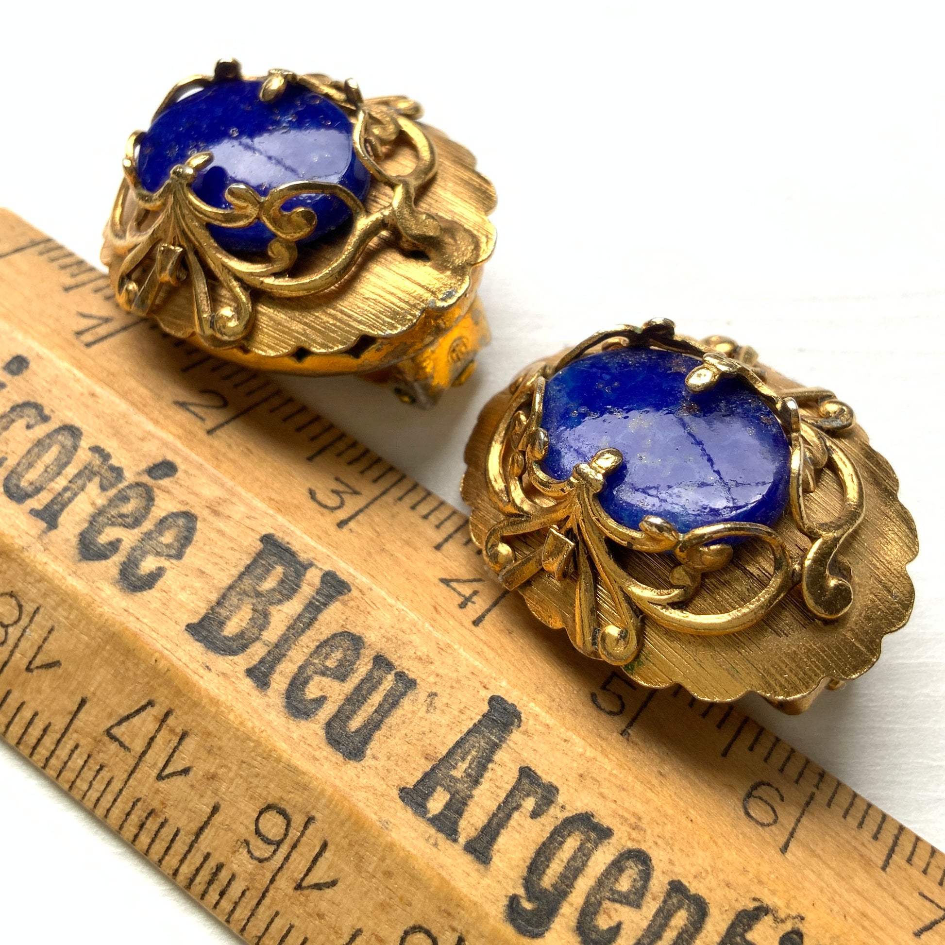 Vibrant blue lapis glass clip-on earrings set in gold-tone metal frames. 鮮やかなブルーのラピスグラスが、ゴールドトーンメタルのフレームに収められたクリップイヤリング。 