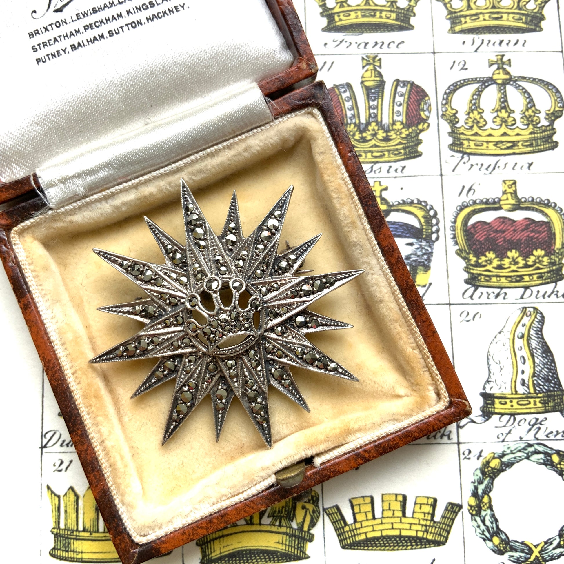 A silver brooch featuring a small crown at the centre of a starburst design. スターバーストの中央に小さな王冠があしらわれた、シルバー製のブローチ。