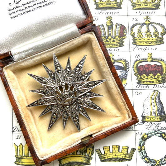A silver brooch featuring a small crown at the centre of a starburst design. スターバーストの中央に小さな王冠があしらわれた、シルバー製のブローチ。
