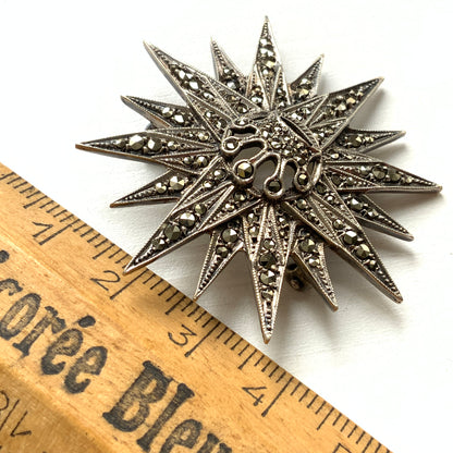 A silver brooch featuring a small crown at the centre of a starburst design. スターバーストの中央に小さな王冠があしらわれた、シルバー製のブローチ。