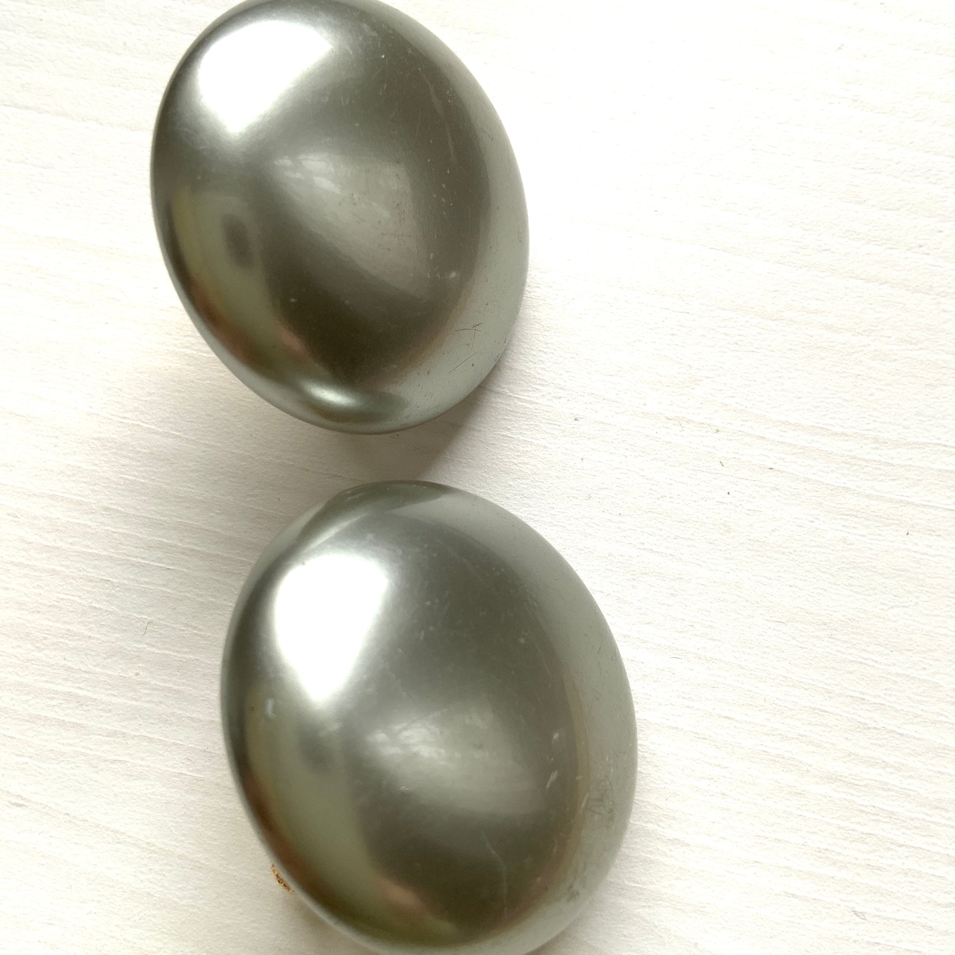 A pair of Napier clip-on earrings featuring large pearl buttons in a deep grey tone. 深みのあるグレーカラーが印象的な、ネイピアの大粒パールボタンのクリップイヤリング。