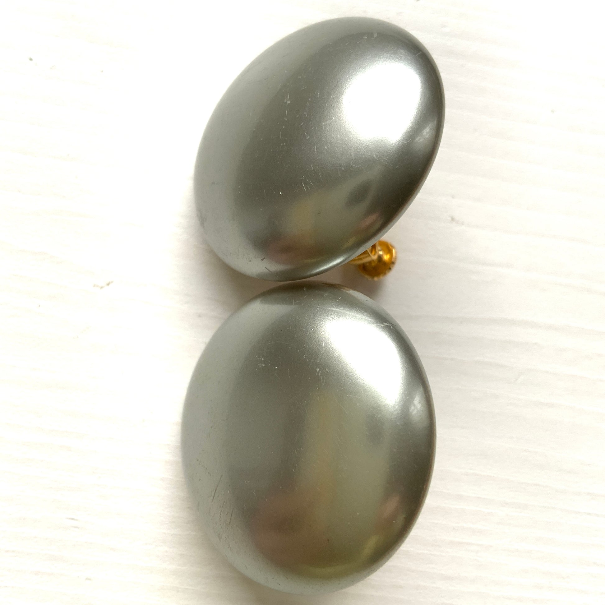 A pair of Napier clip-on earrings featuring large pearl buttons in a deep grey tone. 深みのあるグレーカラーが印象的な、ネイピアの大粒パールボタンのクリップイヤリング。