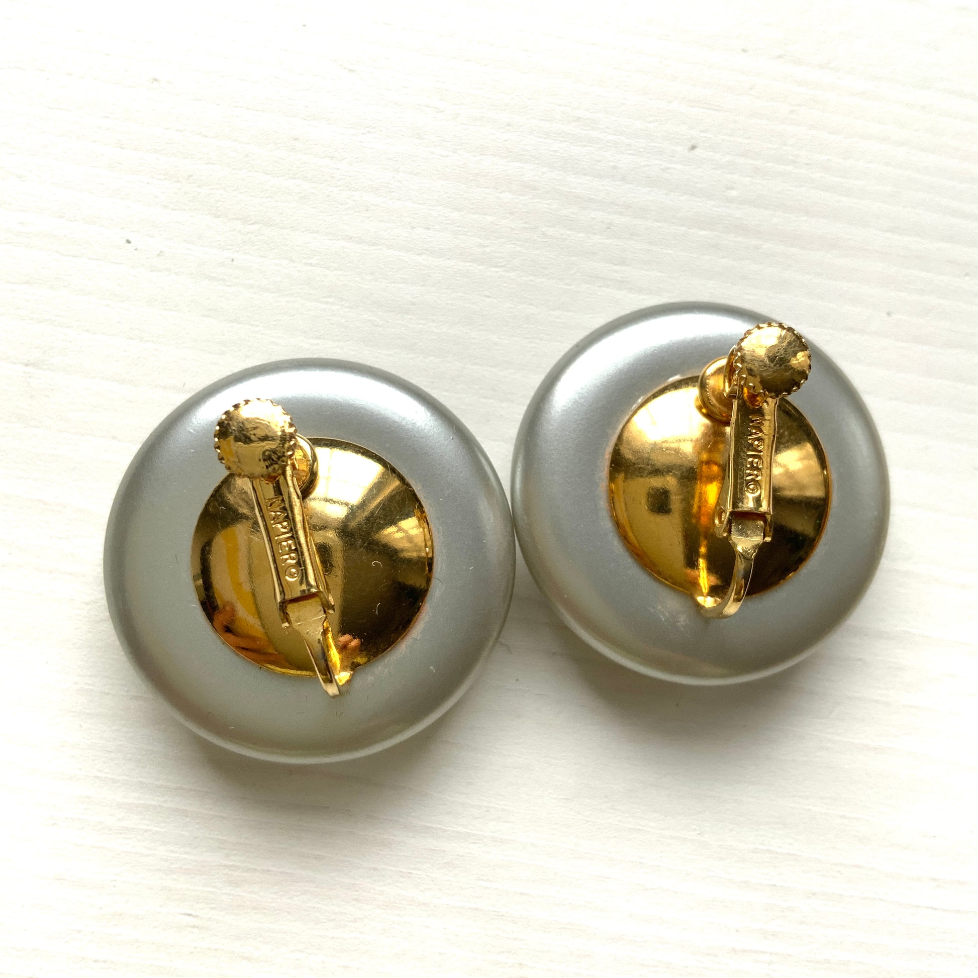 A pair of Napier clip-on earrings featuring large pearl buttons in a deep grey tone. 深みのあるグレーカラーが印象的な、ネイピアの大粒パールボタンのクリップイヤリング。