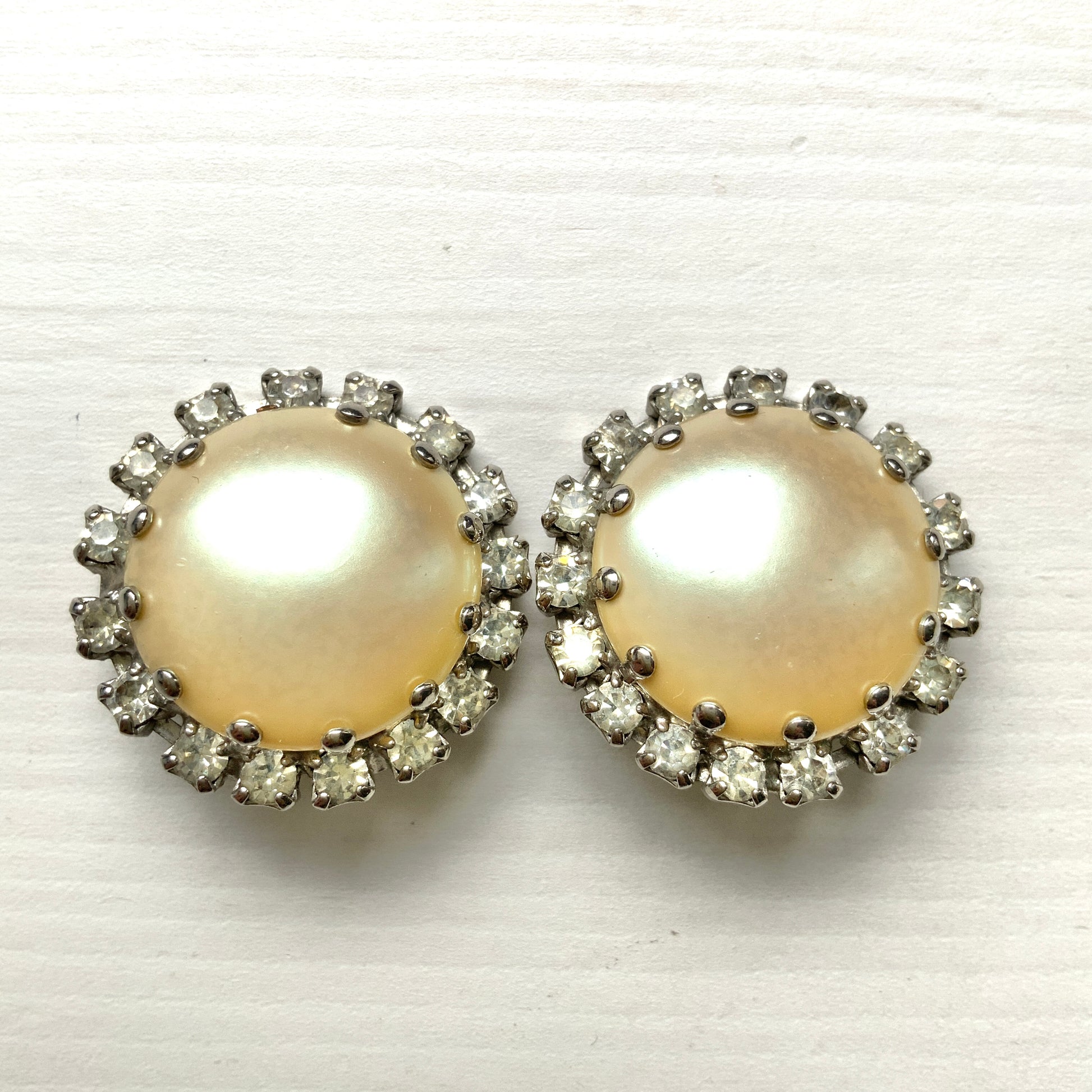 Vintage earrings featuring a flat pearl button surrounded by a halo of clear stones.  フラットなパールボタンの周りを、クリアストーンがぐるりと囲むヴィンテージイヤリング