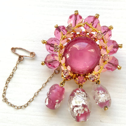 A brooch in soft pink tones, featuring a richly layered design. ピンクのトーンでまとめられた、印象的なデザインのブローチ。