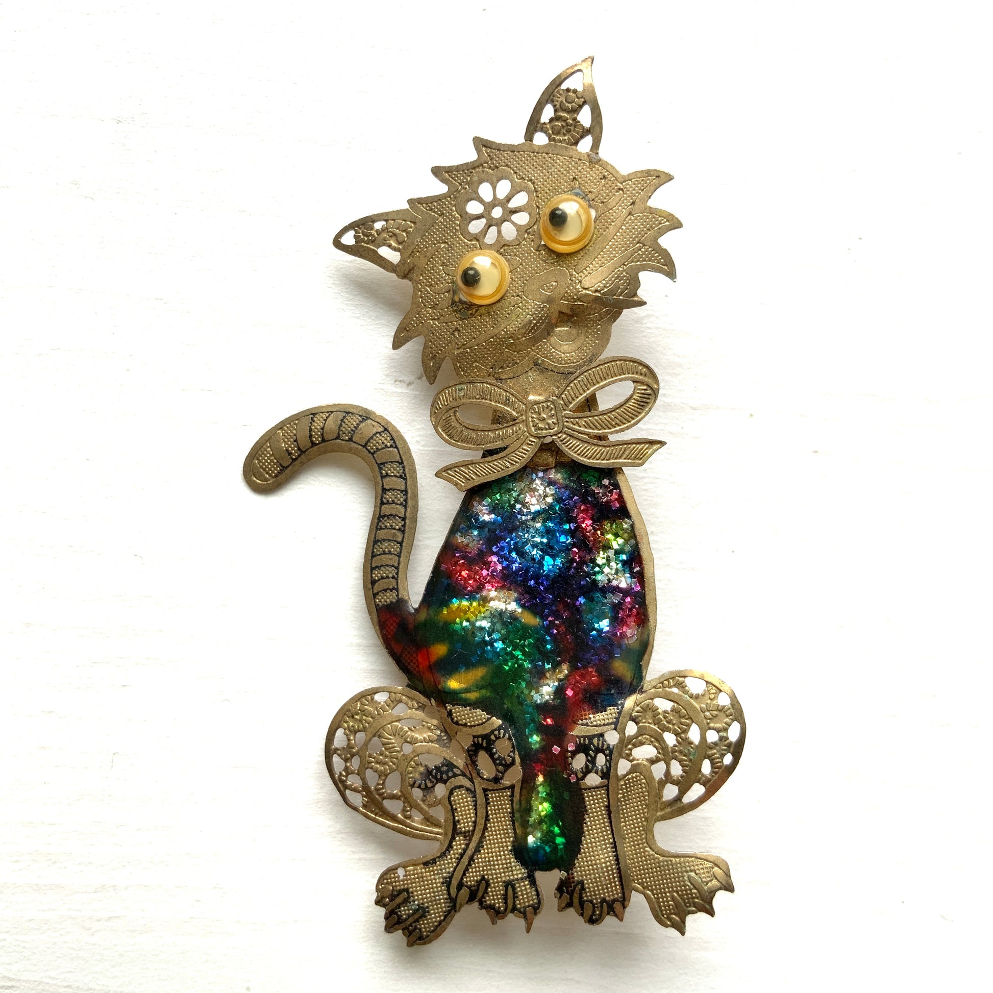 A vintage cat brooch featuring a vibrant rainbow enamel body. レインボーグリッターのボディが印象的な、ヴィンテージのキャットブローチ。