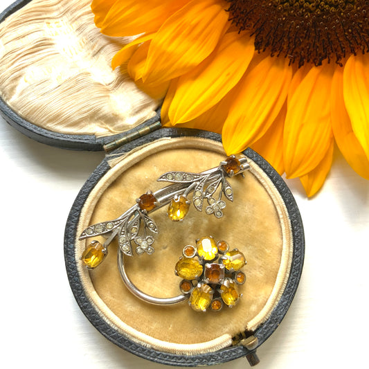 A vintage brooch featuring a large amber glass flower, accented with oval amber glass stones and clusters of small clear rhinestone flowers. アンバーグラスの大輪の花に、同じくアンバーのオーバルグラスと、クリアラインストーンの小さな花々が添えられたブローチ。