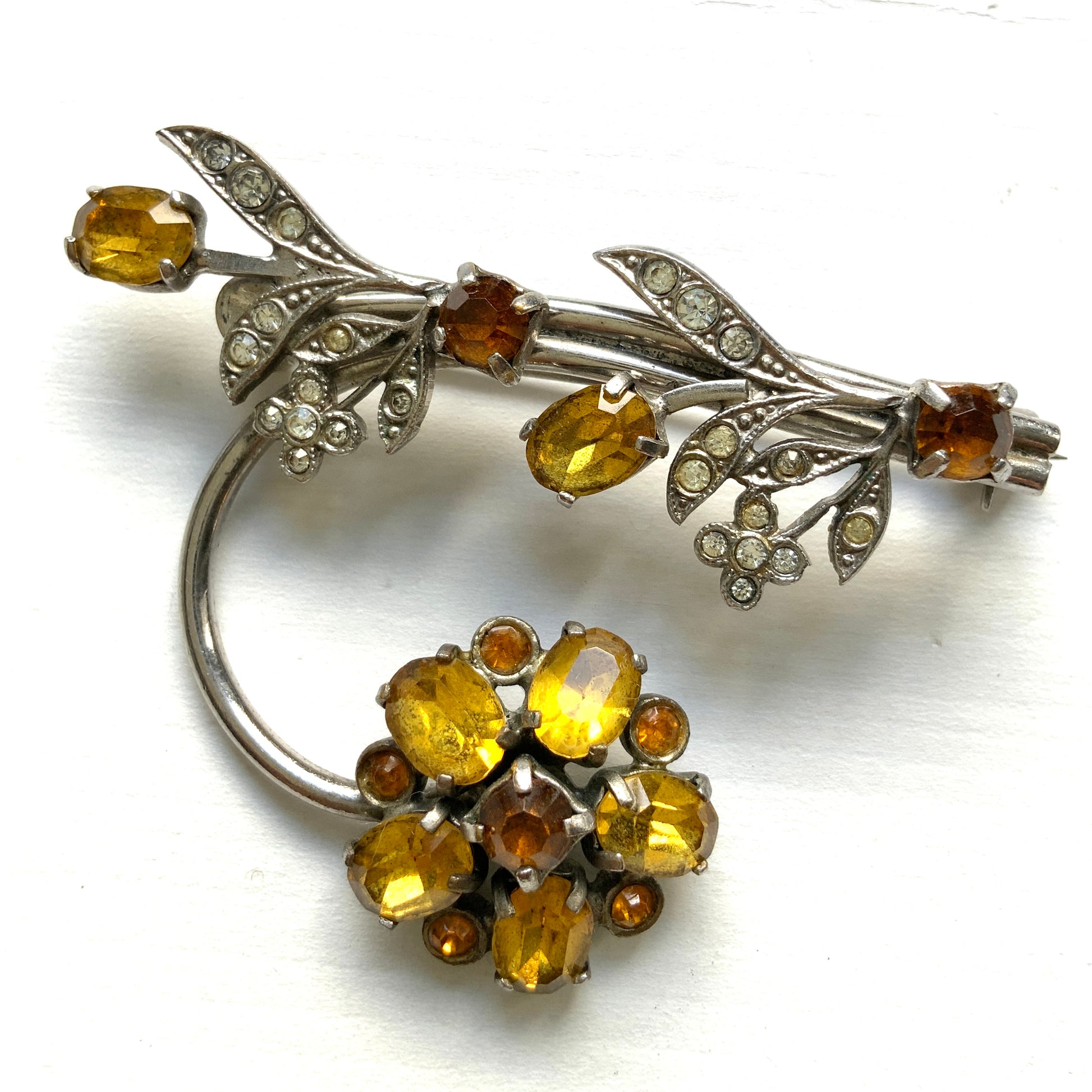 A vintage brooch featuring a large amber glass flower, accented with oval amber glass stones and clusters of small clear rhinestone flowers. アンバーグラスの大輪の花に、同じくアンバーのオーバルグラスと、クリアラインストーンの小さな花々が添えられたブローチ。