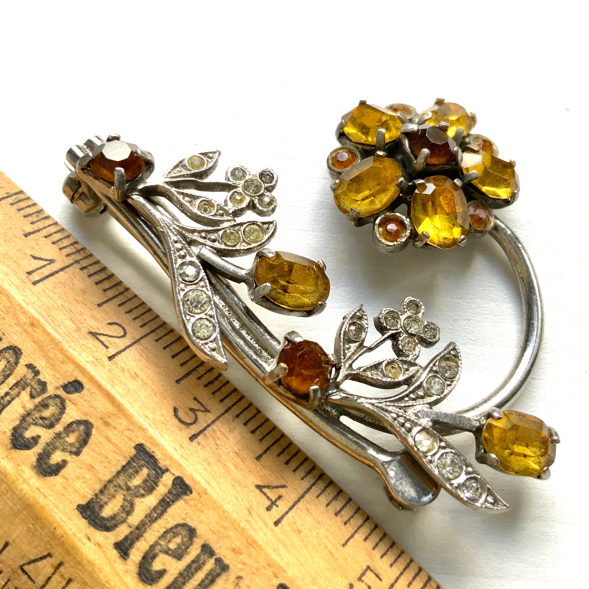 A vintage brooch featuring a large amber glass flower, accented with oval amber glass stones and clusters of small clear rhinestone flowers. アンバーグラスの大輪の花に、同じくアンバーのオーバルグラスと、クリアラインストーンの小さな花々が添えられたブローチ。