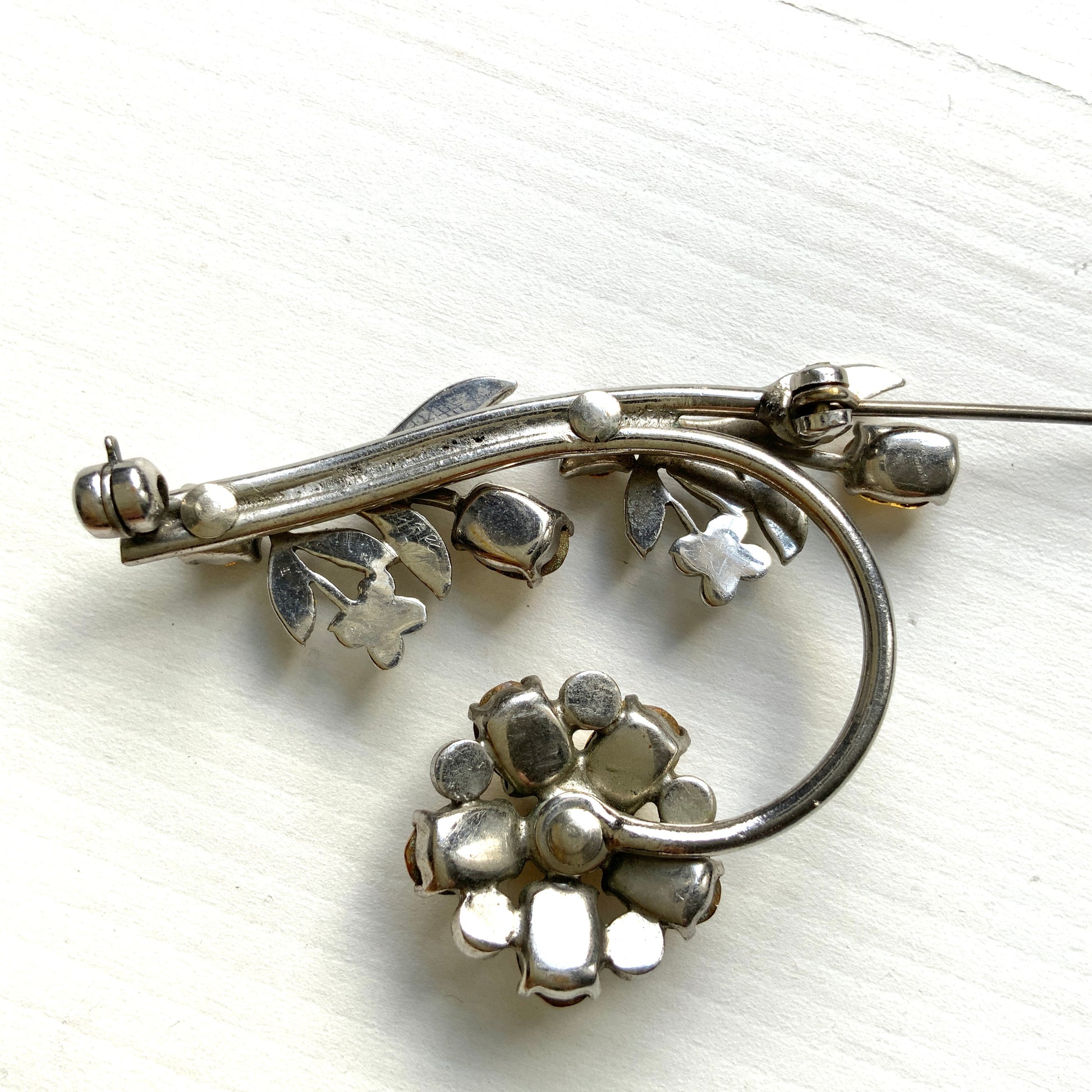 A vintage brooch featuring a large amber glass flower, accented with oval amber glass stones and clusters of small clear rhinestone flowers. アンバーグラスの大輪の花に、同じくアンバーのオーバルグラスと、クリアラインストーンの小さな花々が添えられたブローチ。