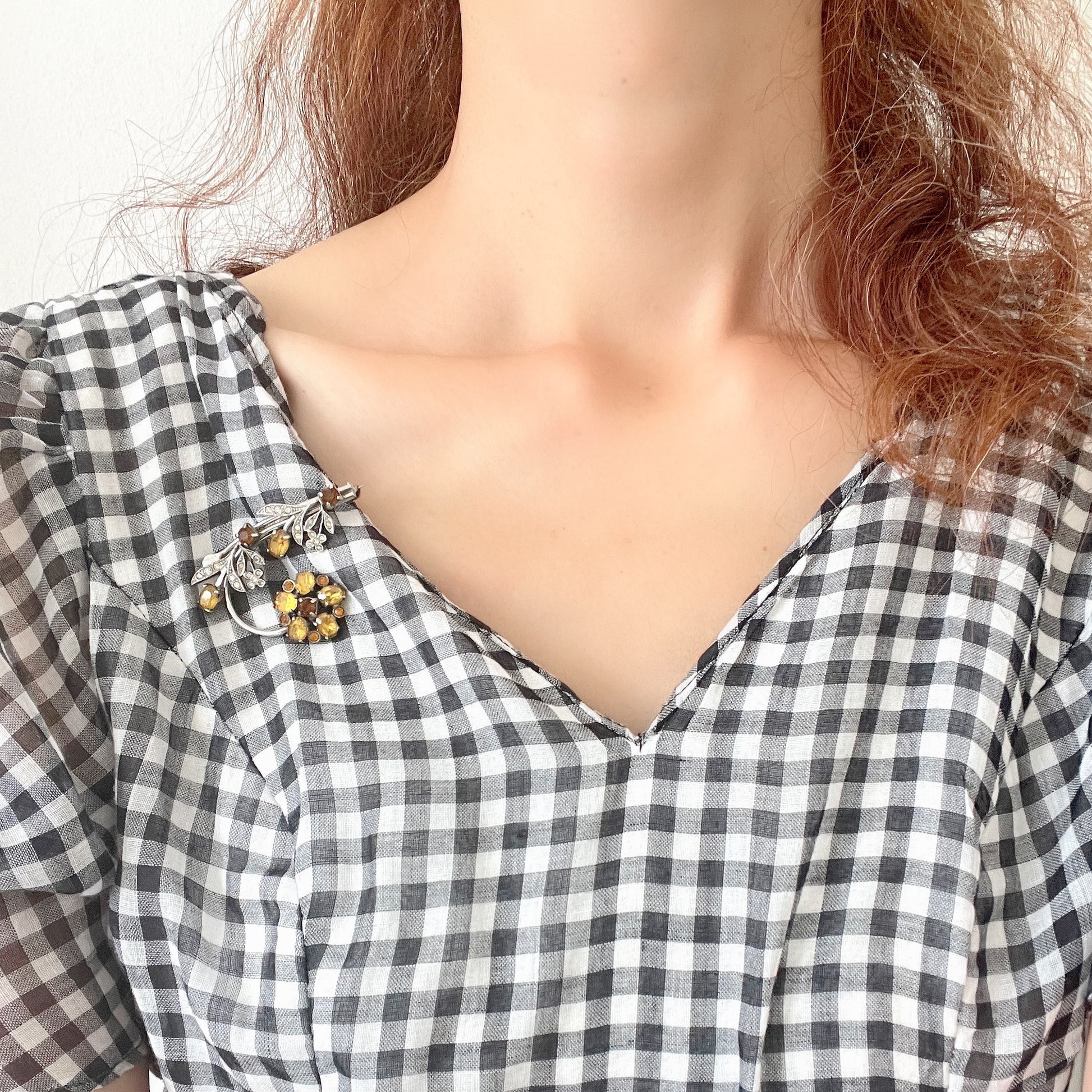 A vintage brooch featuring a large amber glass flower, accented with oval amber glass stones and clusters of small clear rhinestone flowers. アンバーグラスの大輪の花に、同じくアンバーのオーバルグラスと、クリアラインストーンの小さな花々が添えられたブローチ。