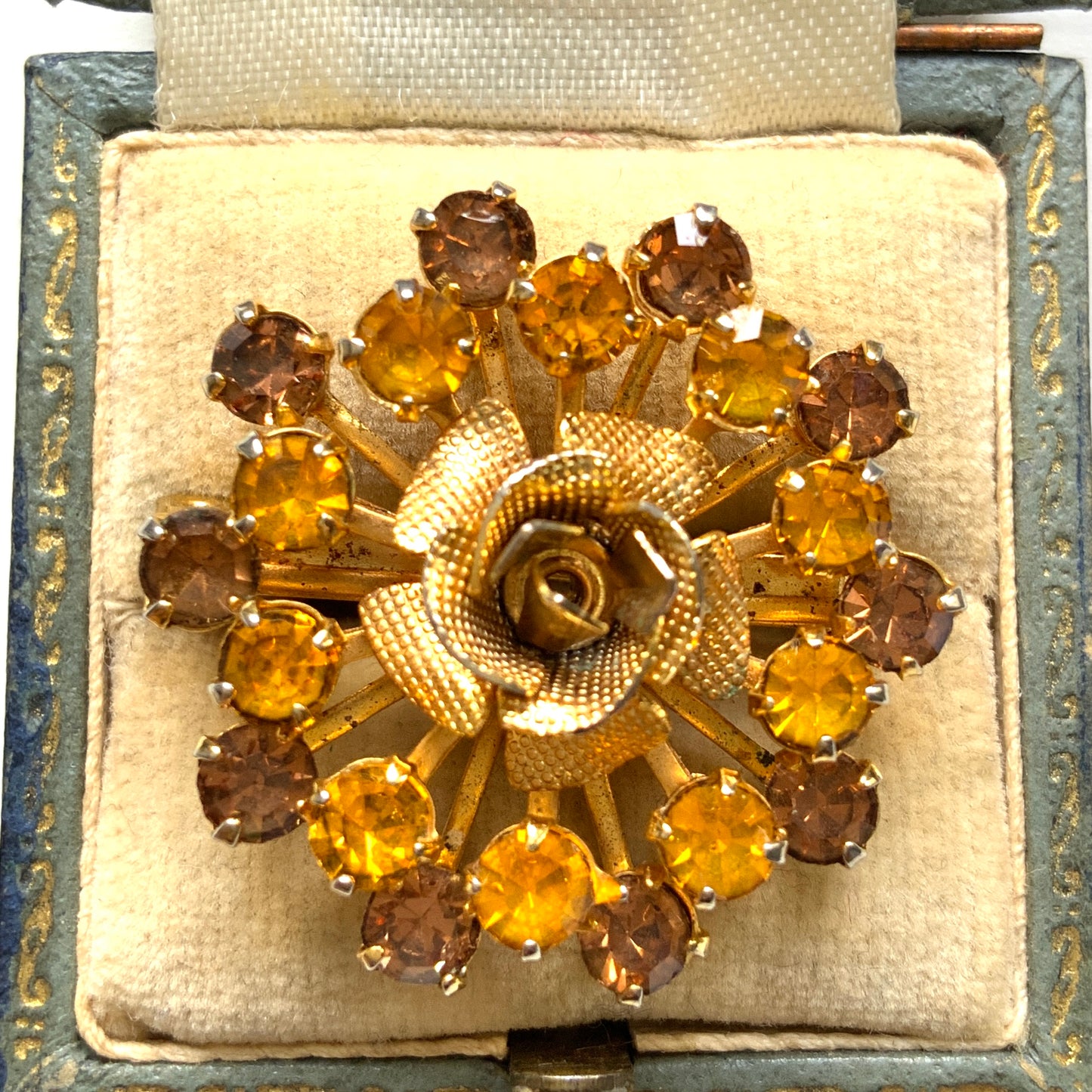 A vintage brooch featuring a small gold-tone rose, with two-tone amber rhinestones sparkling out like a burst of light. ゴールドトーンの小さなバラから２トーンのアンバーラインストーンがスパークしているようなブローチ。