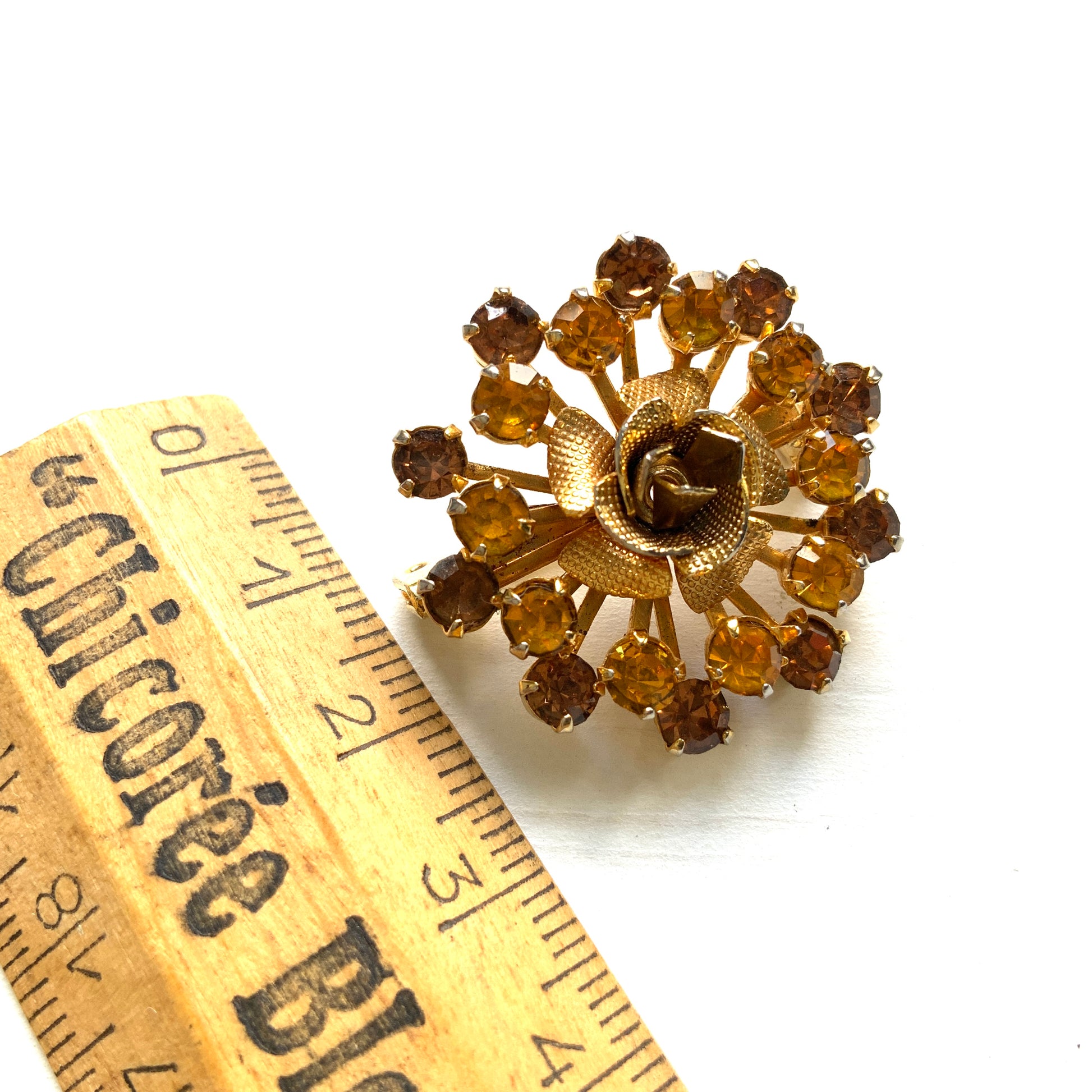 A vintage brooch featuring a small gold-tone rose, with two-tone amber rhinestones sparkling out like a burst of light. ゴールドトーンの小さなバラから２トーンのアンバーラインストーンがスパークしているようなブローチ。