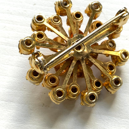 A vintage brooch featuring a small gold-tone rose, with two-tone amber rhinestones sparkling out like a burst of light. ゴールドトーンの小さなバラから２トーンのアンバーラインストーンがスパークしているようなブローチ。