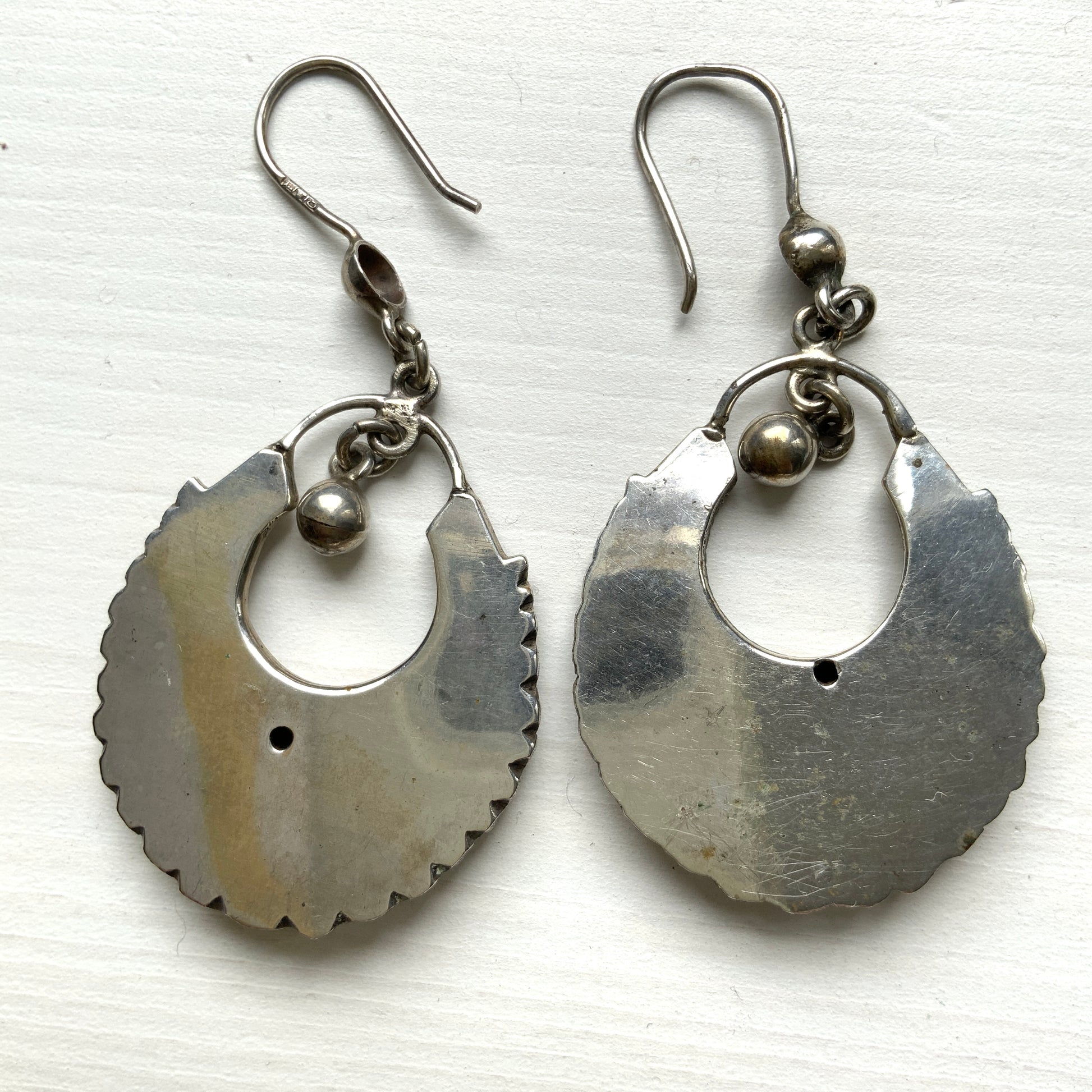 Striking silver tone hoop earrings with geometric embossed patterns and granulated bead details. 半月型にジオメトリックな打ち出し模様と粒状の装飾を施した、存在感あるシルバートーンのフープピアス。