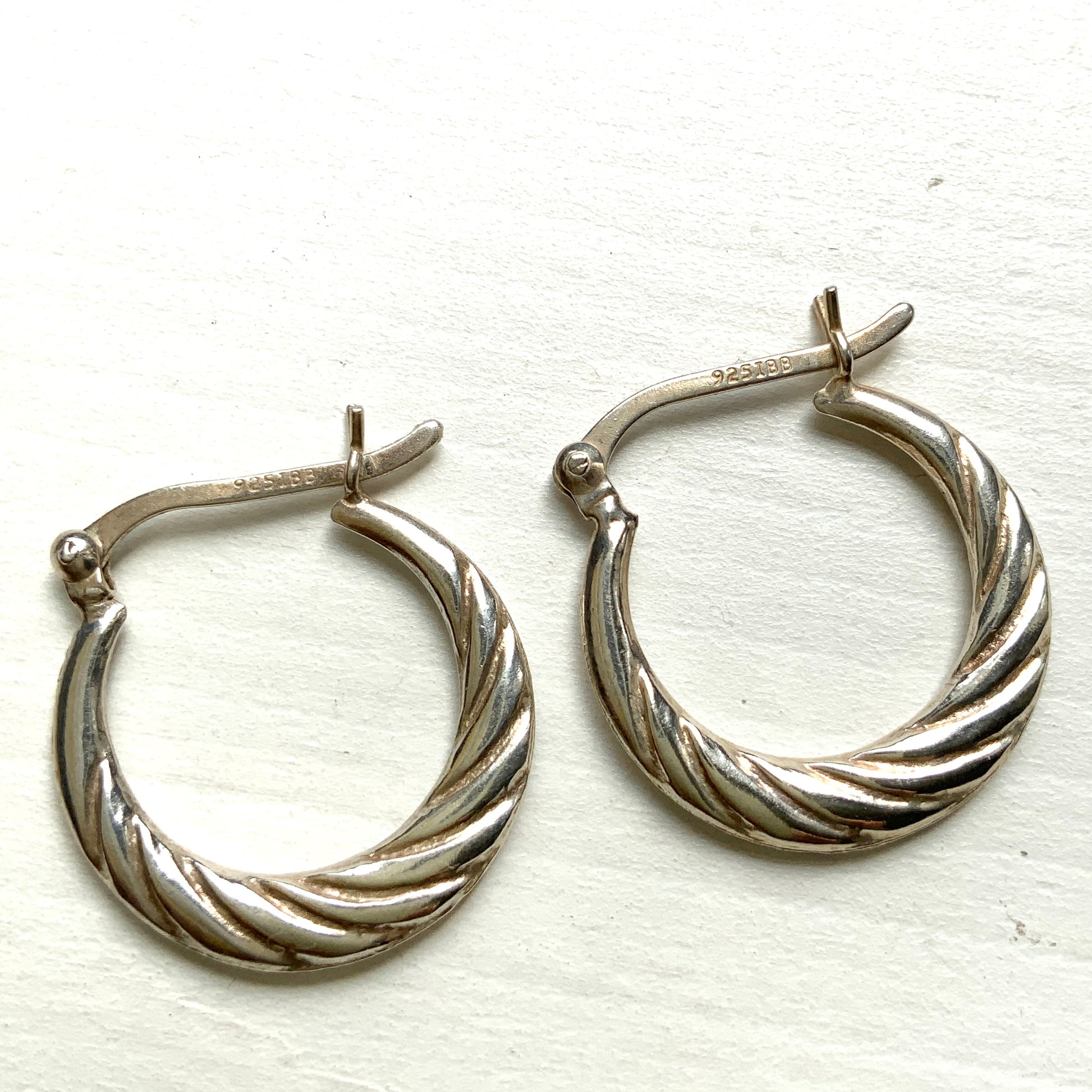 Silver hoop earrings with a twisted design.  シルバーのツイスト模様が入ったフープピアス。 