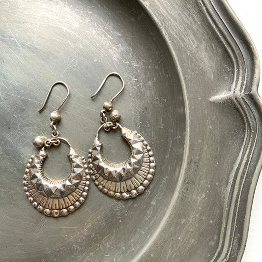 Striking silver tone hoop earrings with geometric embossed patterns and granulated bead details. 半月型にジオメトリックな打ち出し模様と粒状の装飾を施した、存在感あるシルバートーンのフープピアス。