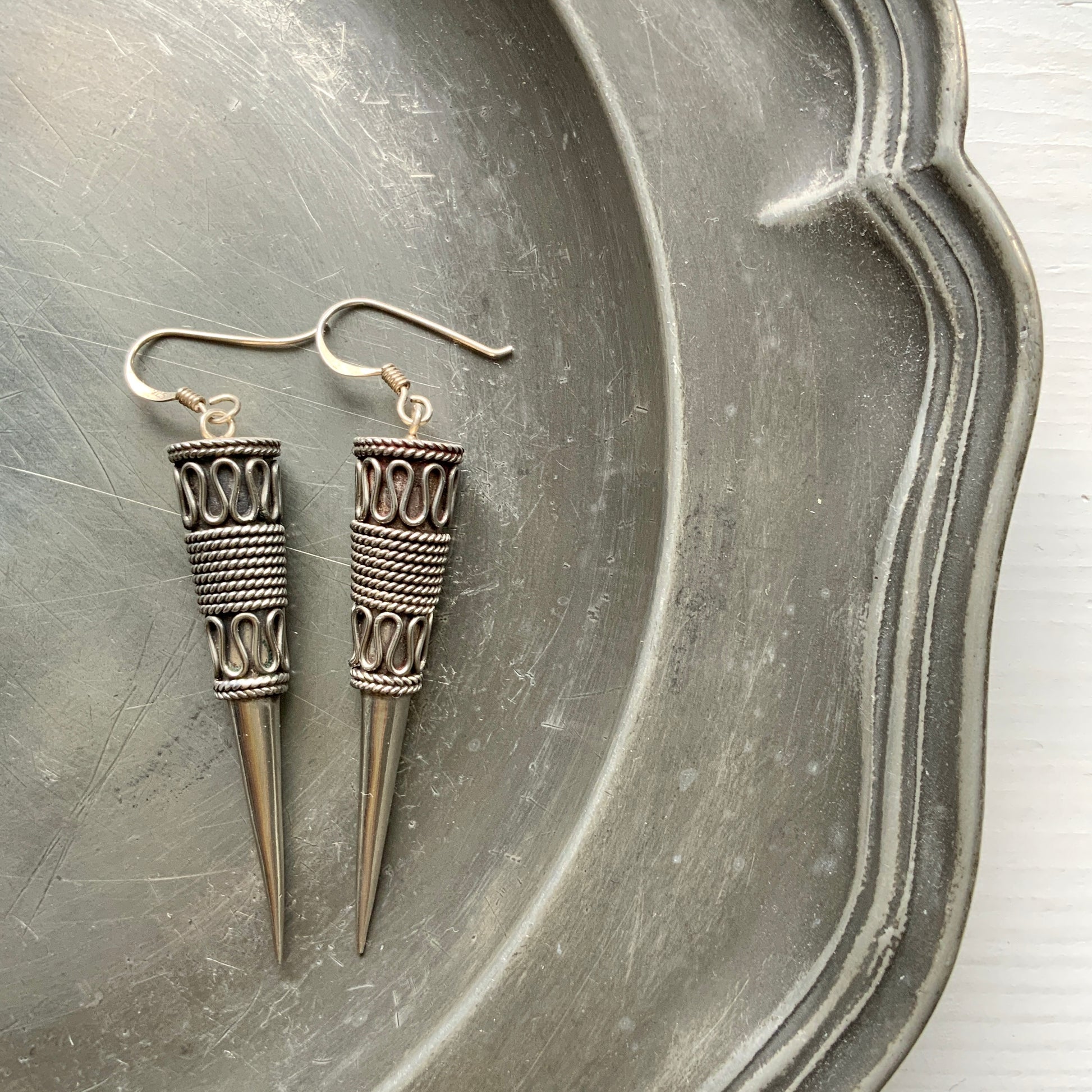 Silver spike-shaped earrings with tribal-inspired patterns.  トライバルな模様が入った細長いスパイク型のシルバーピアス。